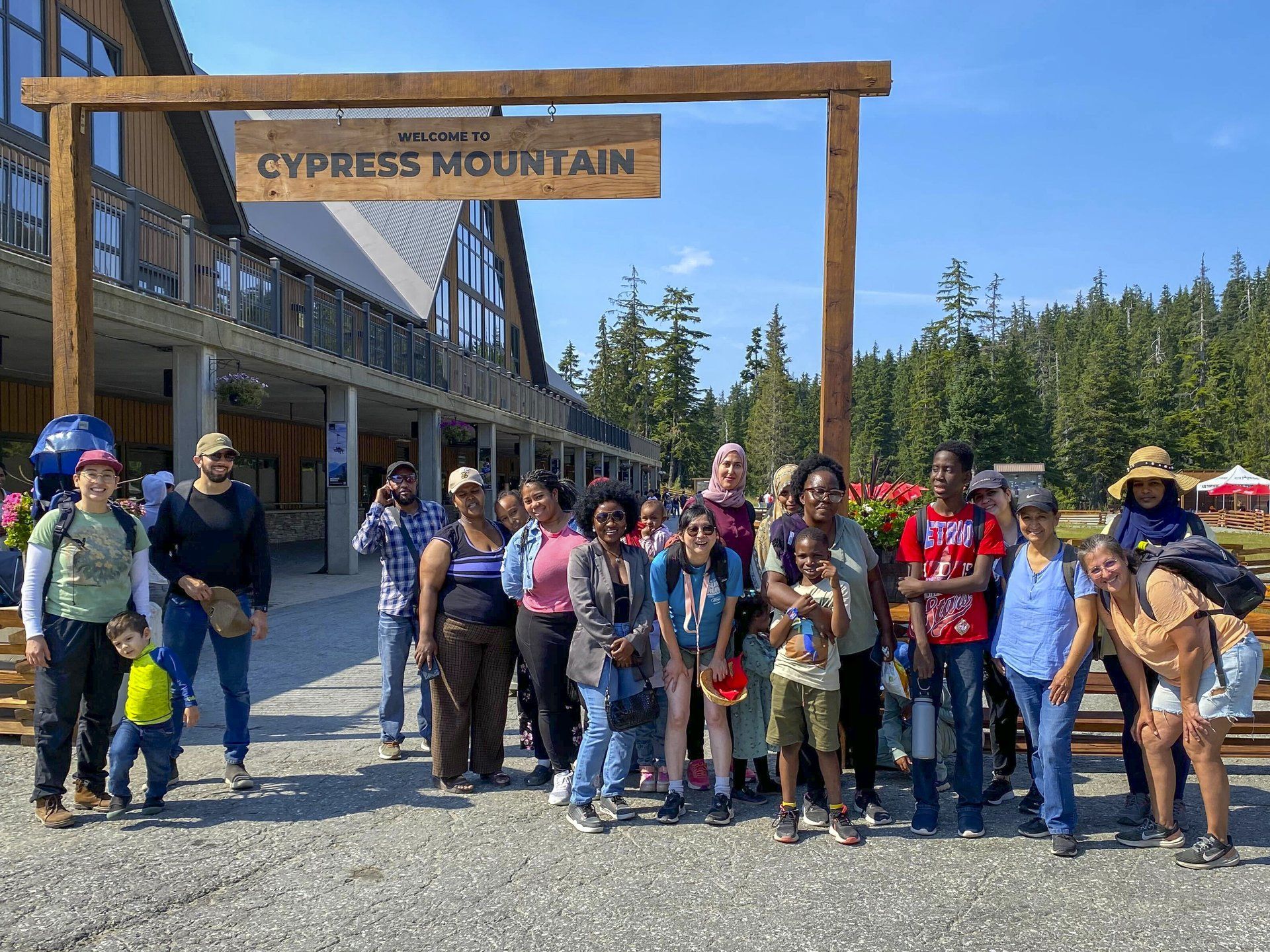 Group of people standing under a “Welcome to Cypress Mountain” sign outdoors.