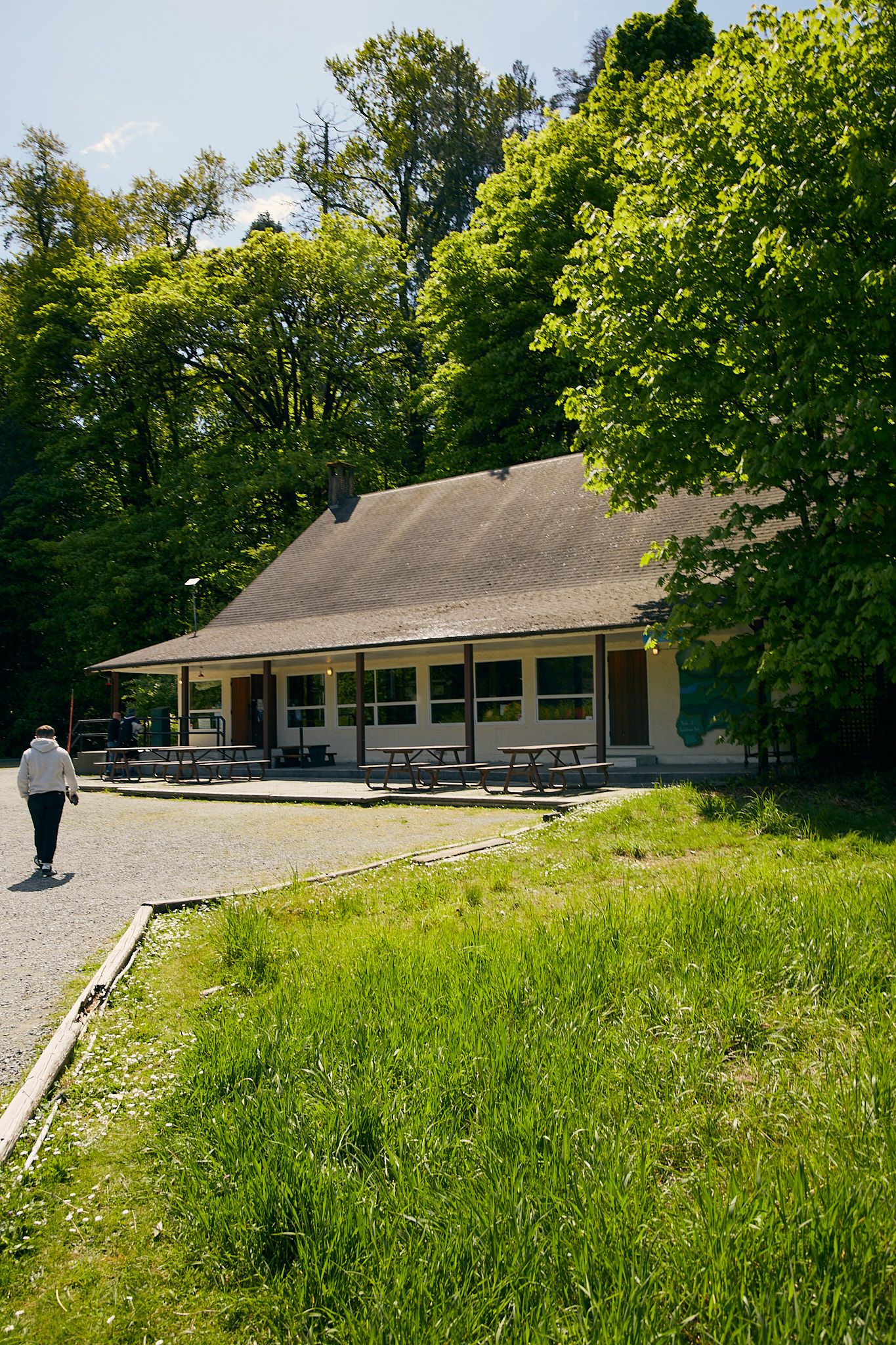 Goldstream Nature House on a sunny day, with picnic tables and leafy green trees outside.