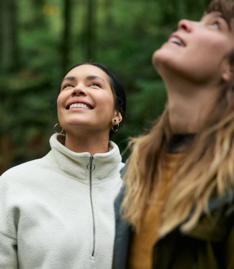 Two people smile and look up to the sky in a forest setting