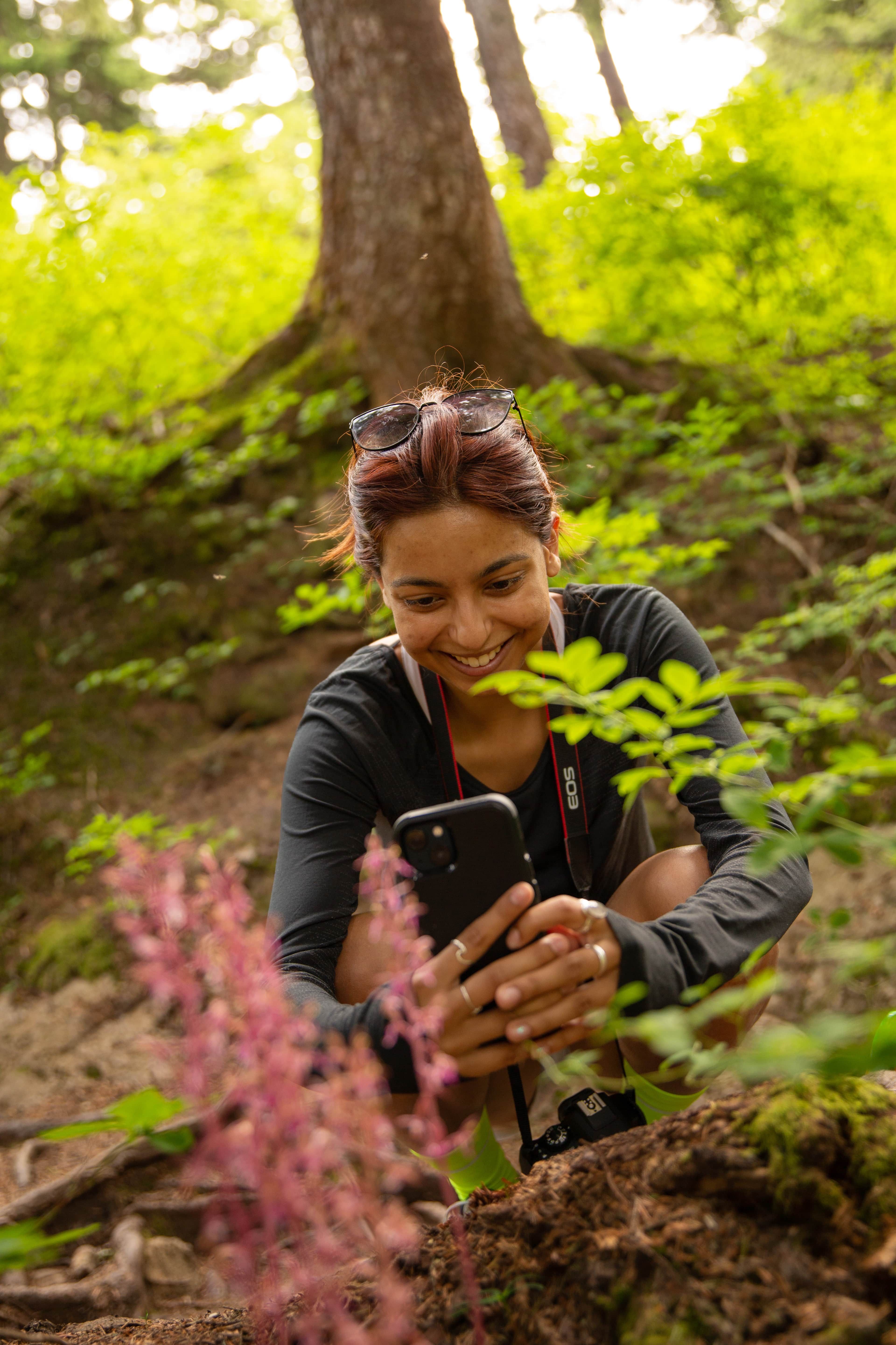 A smiling person captures a photo of flowers with their phone