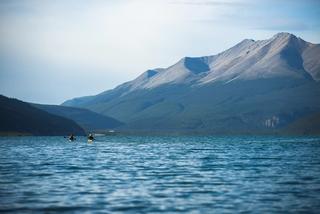 Two kayakers drift across wide open water, with mountains seen in the background