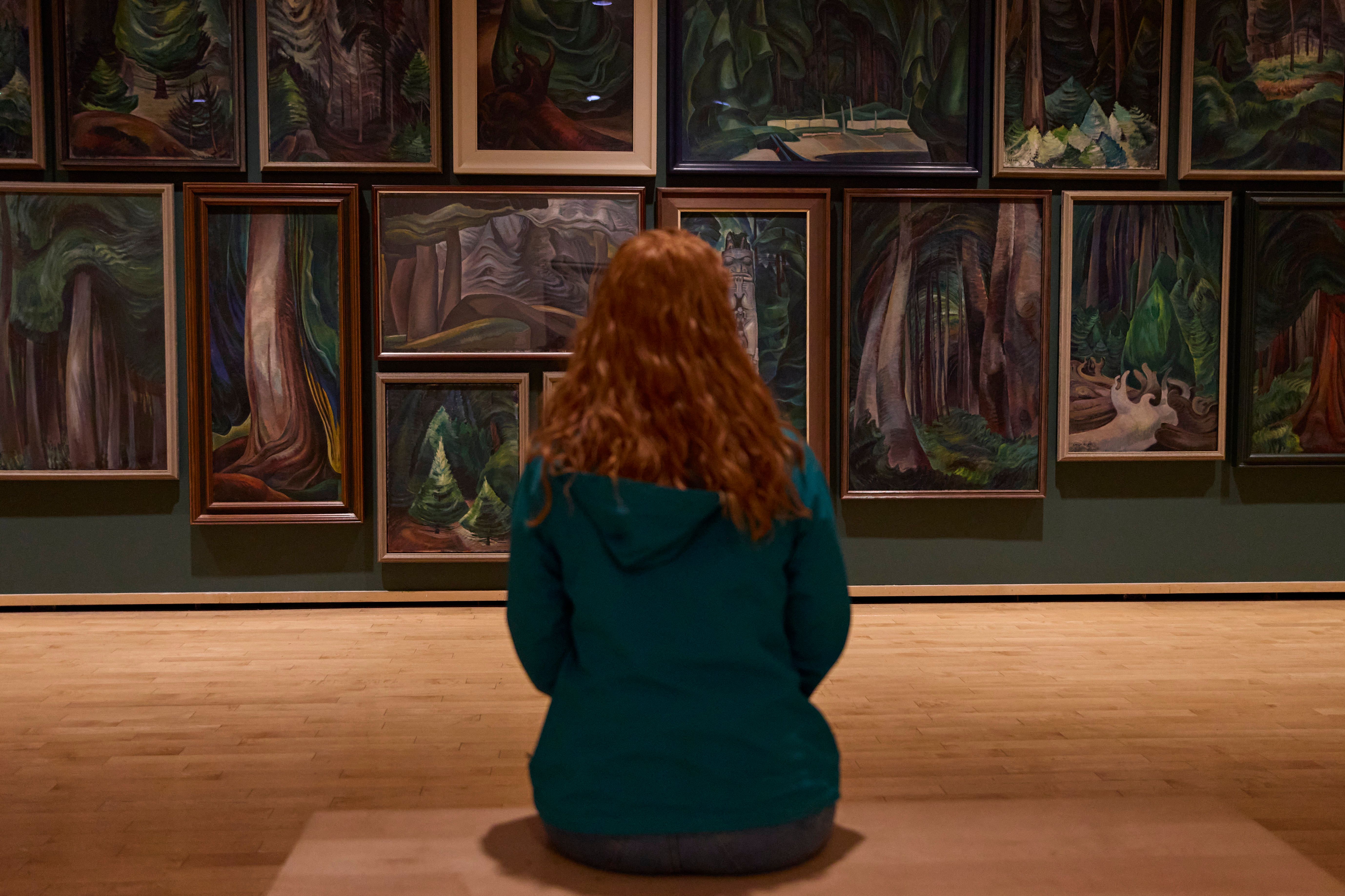 Person sits in an art gallery and looks at Emily Carr paintings