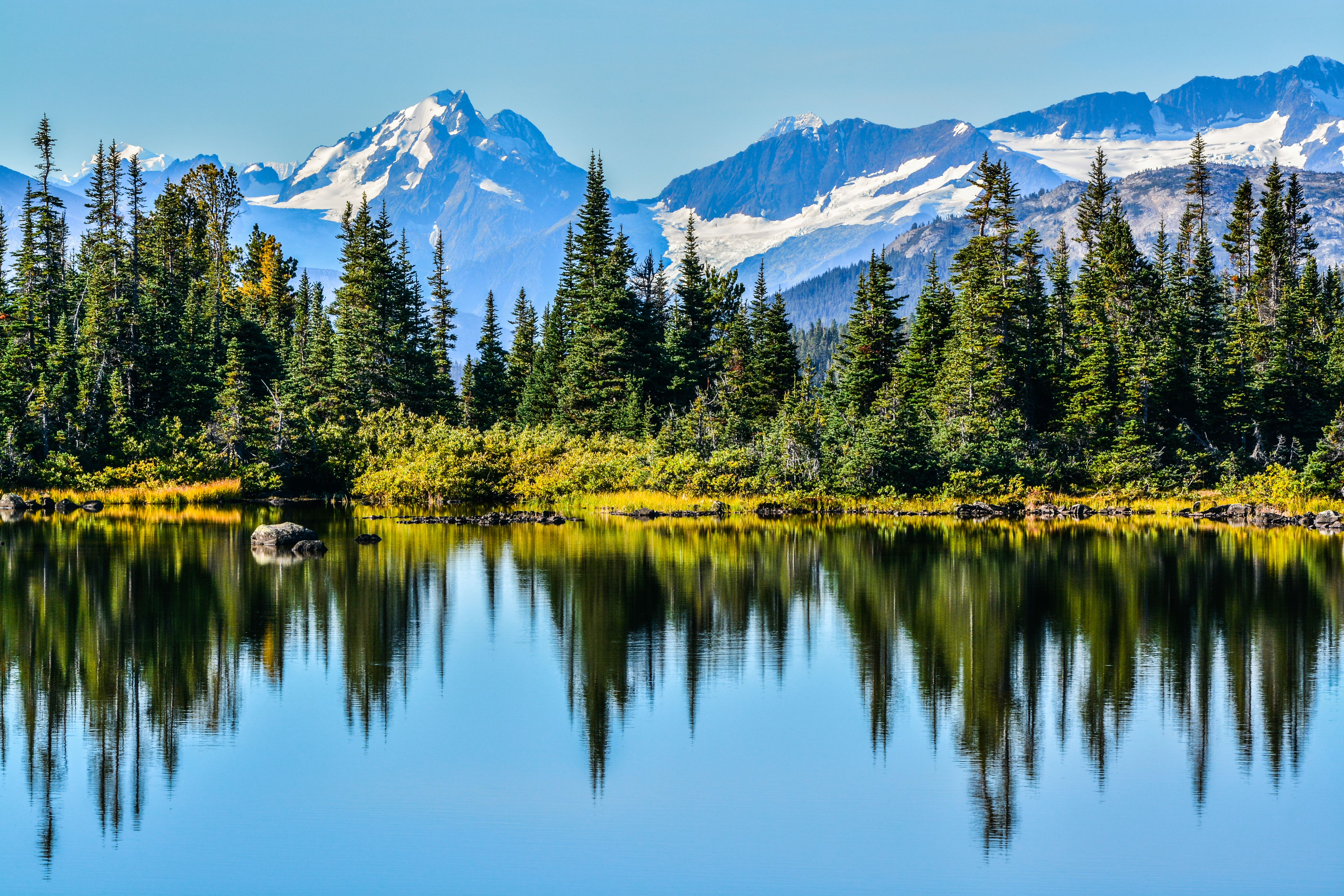 A shimmering lake surrounded by evergreen trees and snowcapped mountains