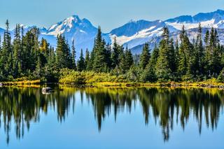 A shimmering lake surrounded by evergreen trees and snowcapped mountains