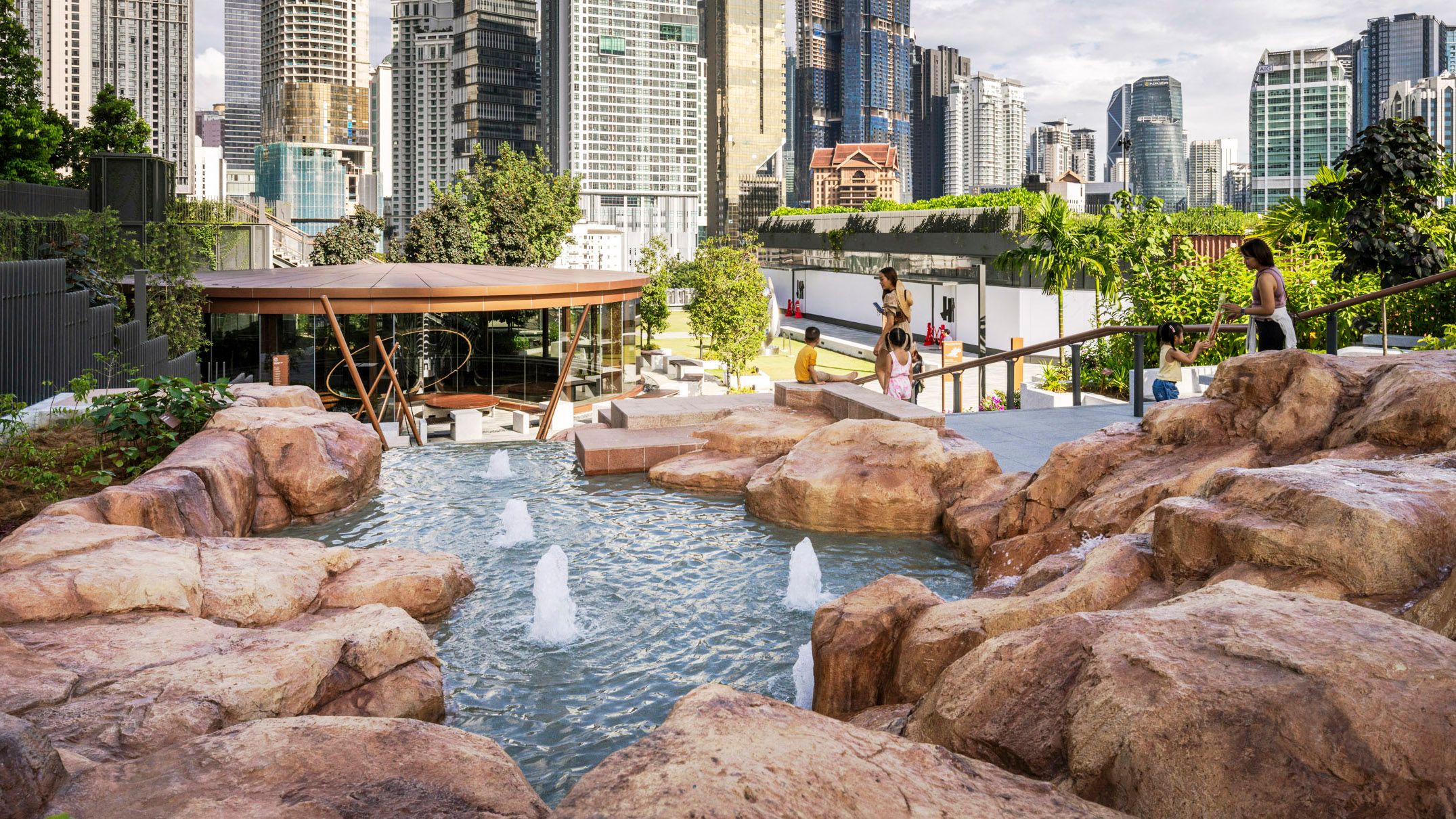 A photo of a rocky water feature in a large rooftop park. City buildings fill the background.