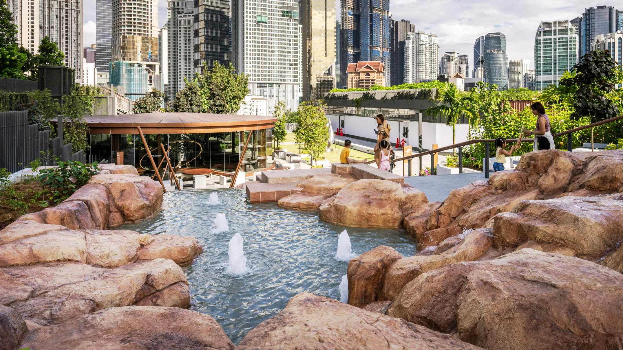 A photo of a rocky water feature in a large rooftop park. City buildings fill the background.