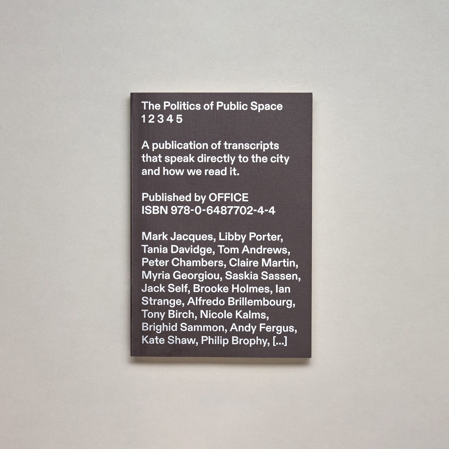 A photo of a black book cover with white text reading "The Politics of Public Space 1 2 3 4 5: A publication of transcripts that speak directly to the city and how we read it."