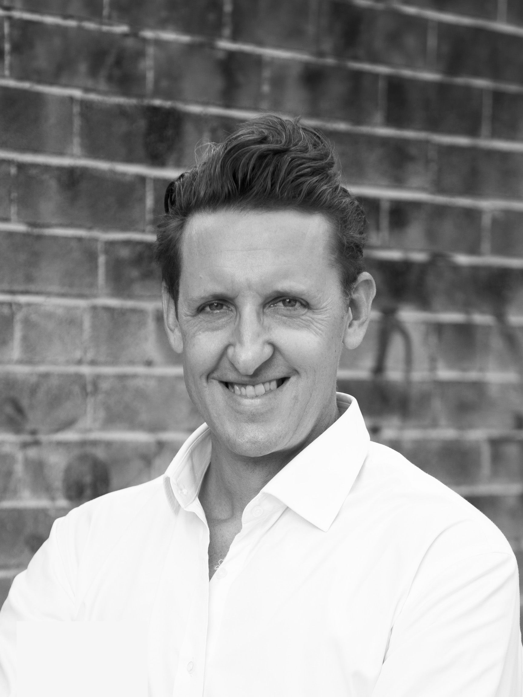 Black and white photo of man in white business shirt against a brick wall.