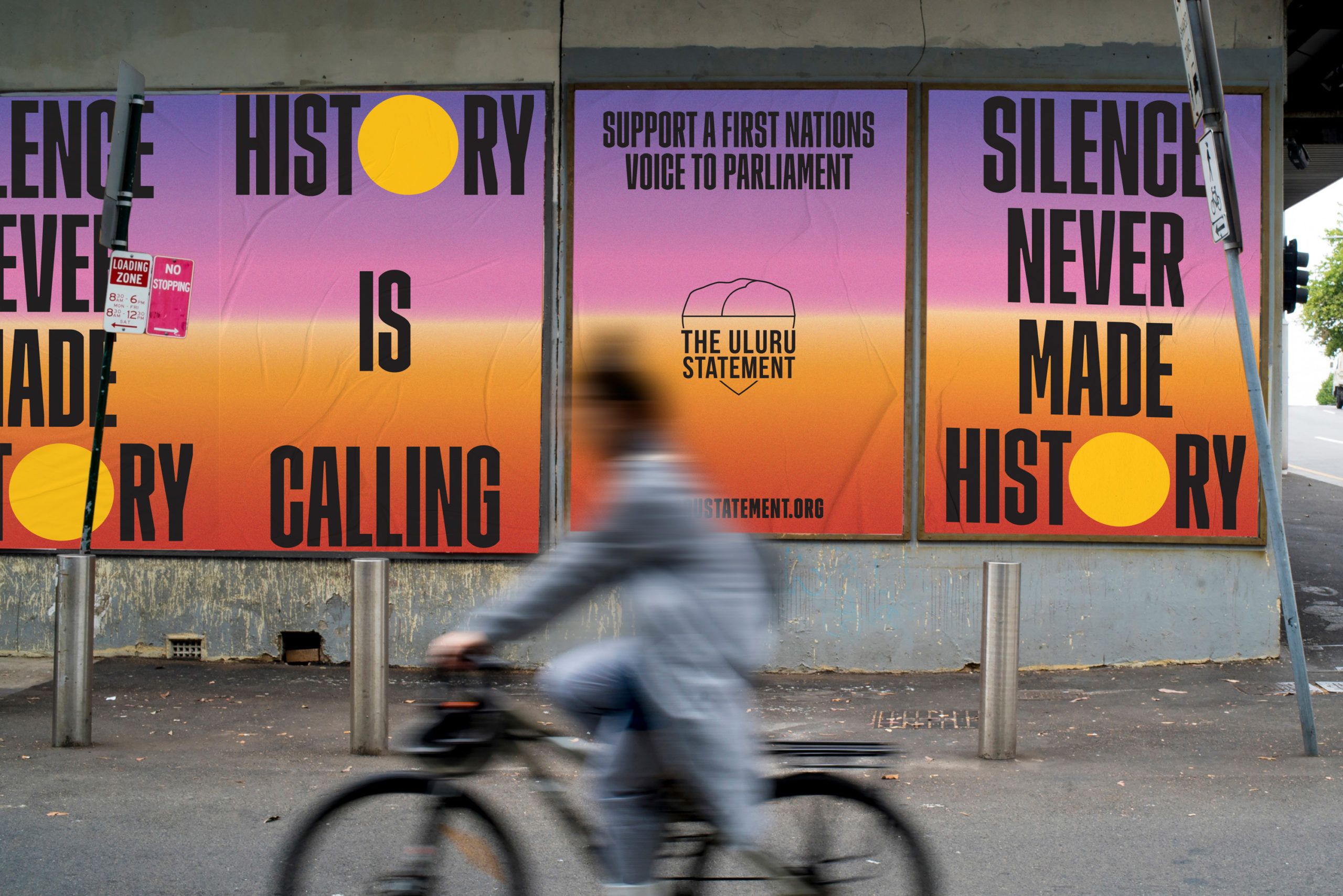 A digital mock-up of Uluru Statement Posters on an urban wall reading "History is Calling" and "Silence Never Made History" with a blurry cyclist passing in the foreground.