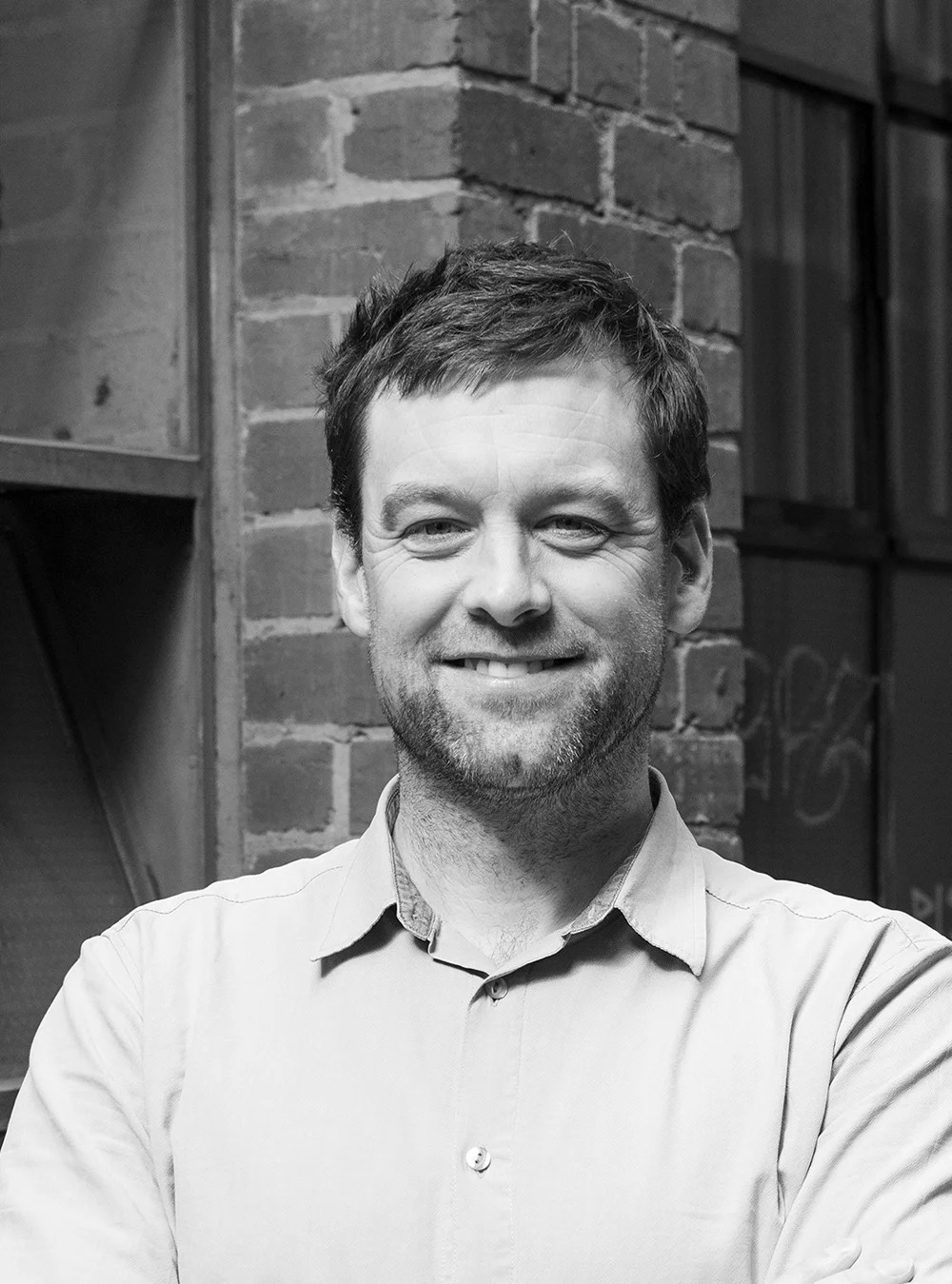 A headshot of a smiling person in-front of an old brick façade.