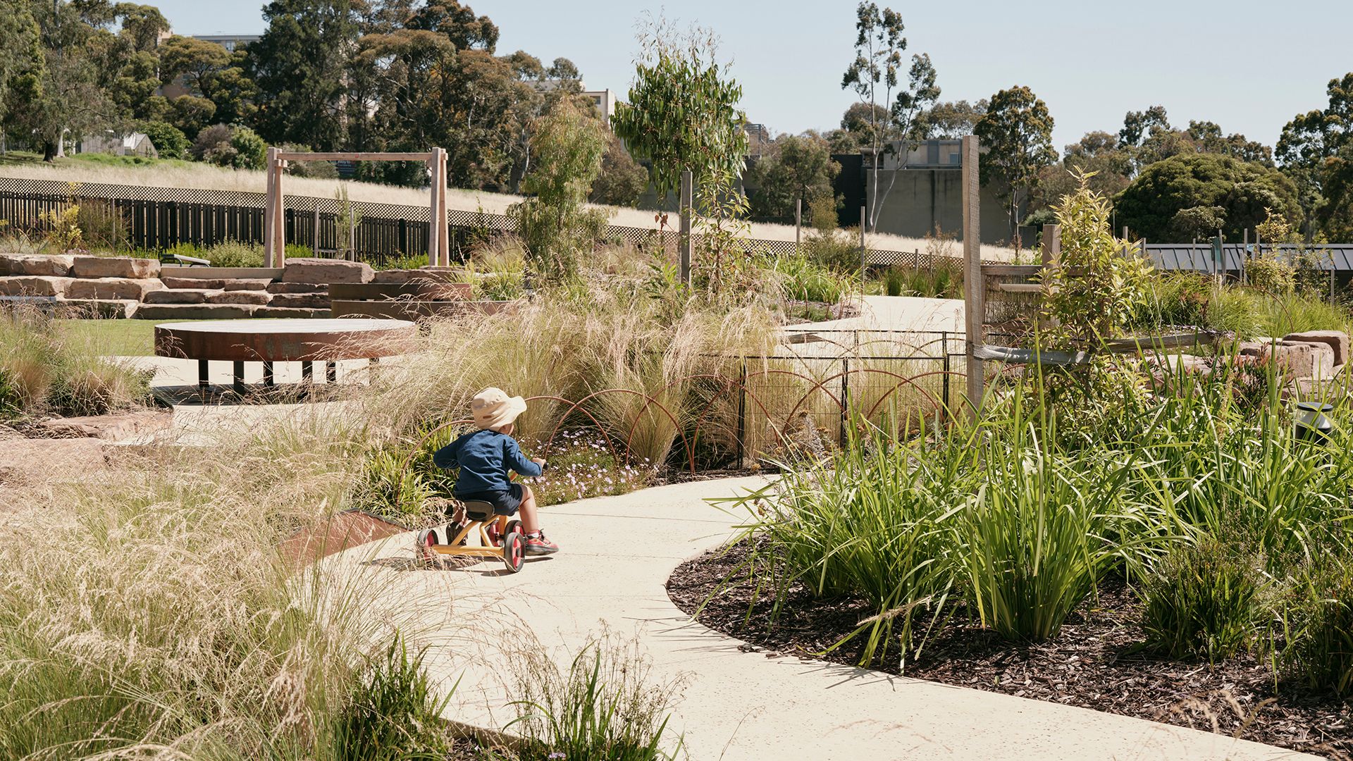 Young child rides his tricycle along a path set within a childcare playground.