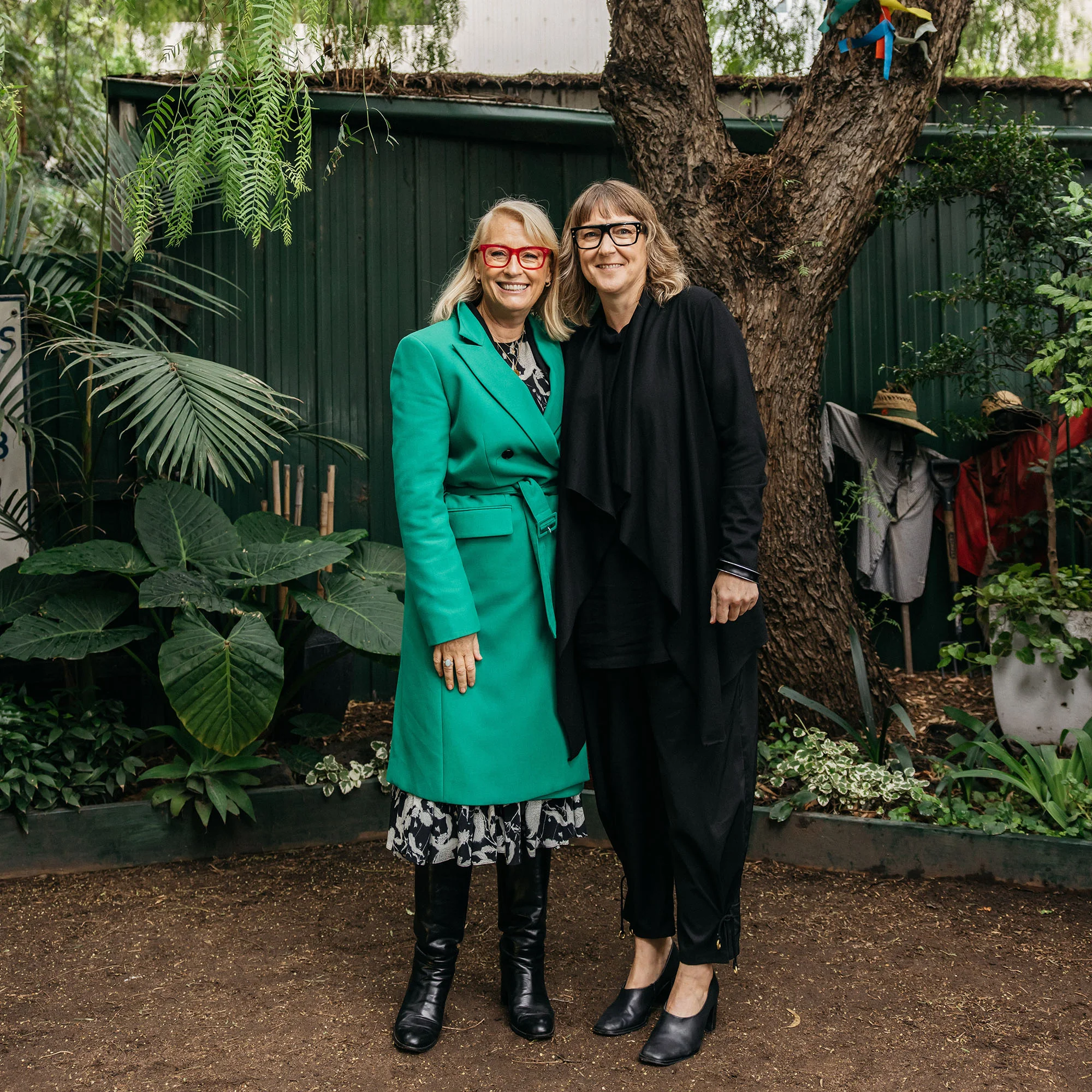 A full length photo of two people smiling for the camera, one is wearing a bright green coat.