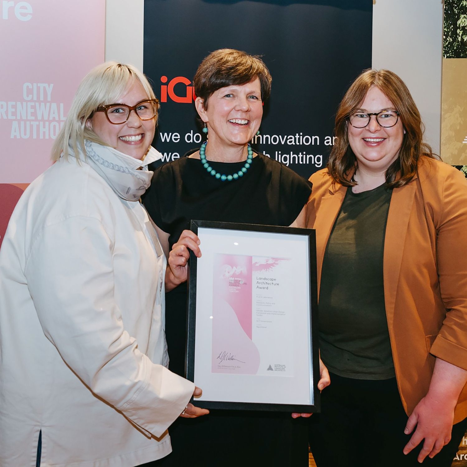 A photo of three people smiling while holding a framed certificate.