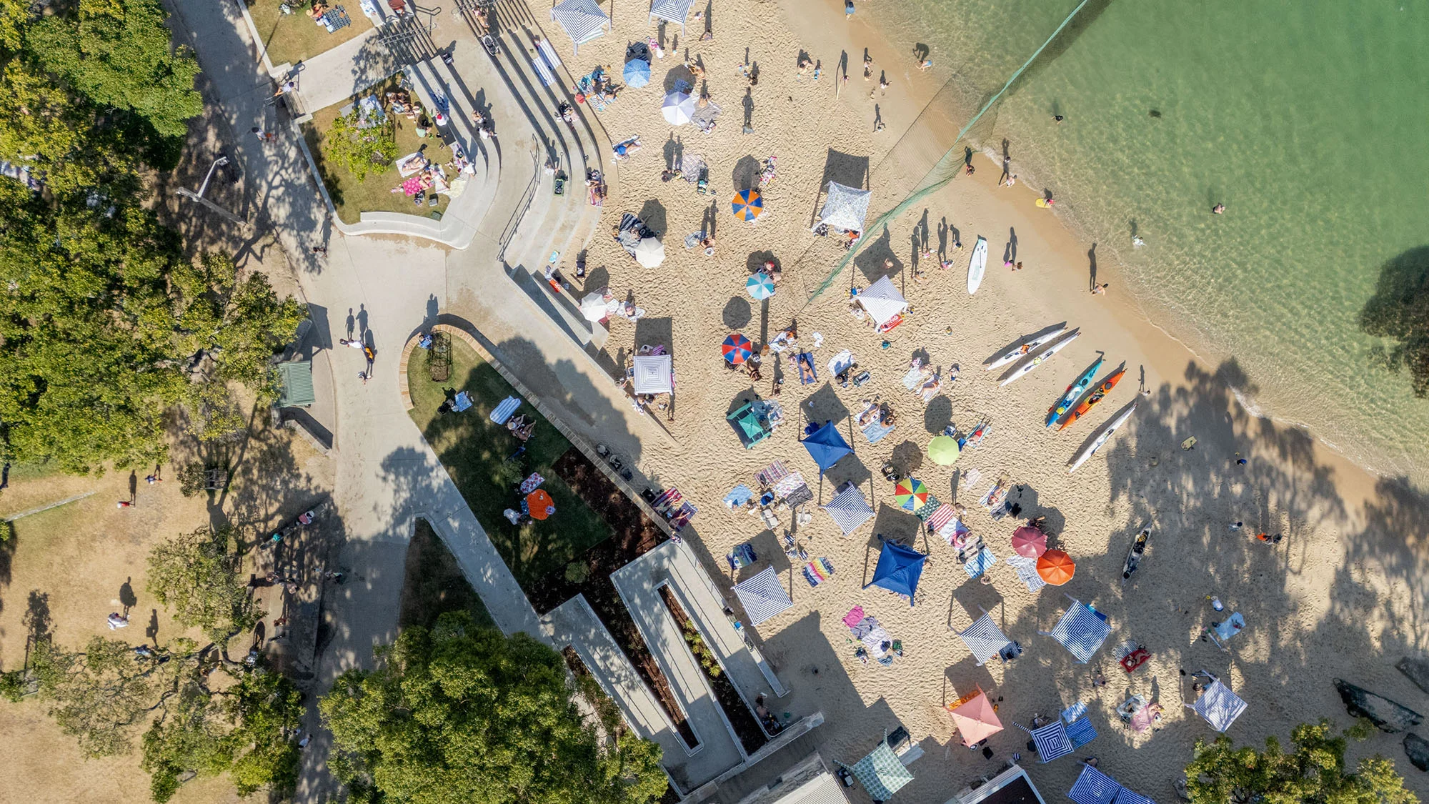 A drone photograph looking down on a sunny beach with a tiered seawall.