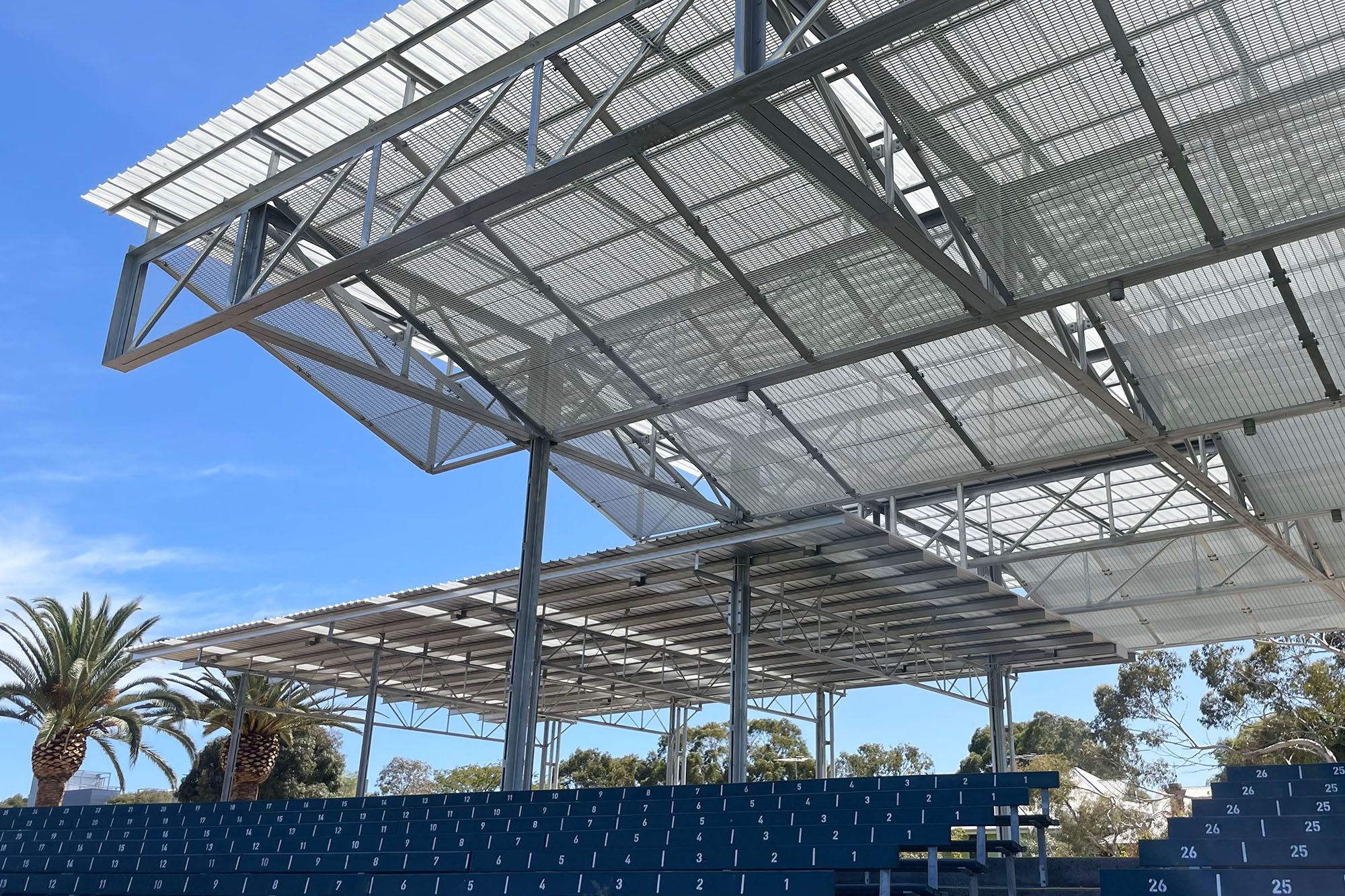 A photo of a sports pavilion with seating below, and blue sky behind.