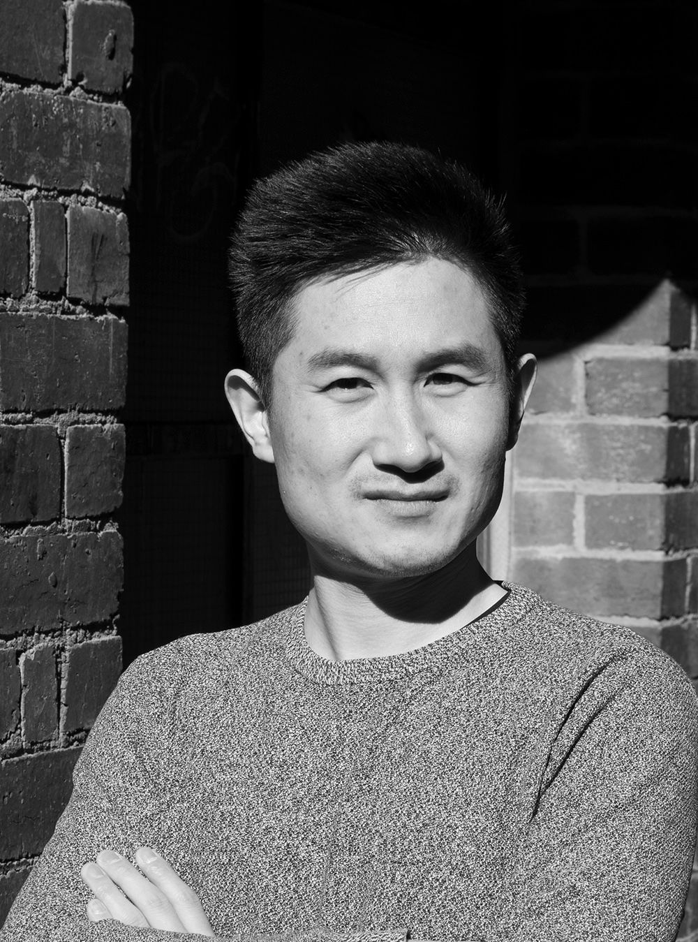 A black and white headshot of a person slightly smiling with their arms crossed.