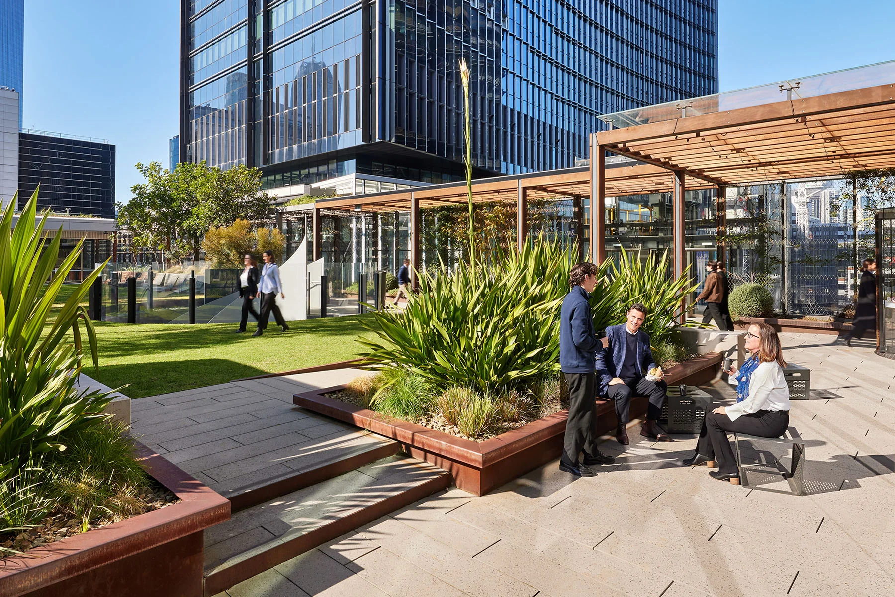 A photo of a handful of people gathering in an urban park. There is a small lawn and a large building in the background.