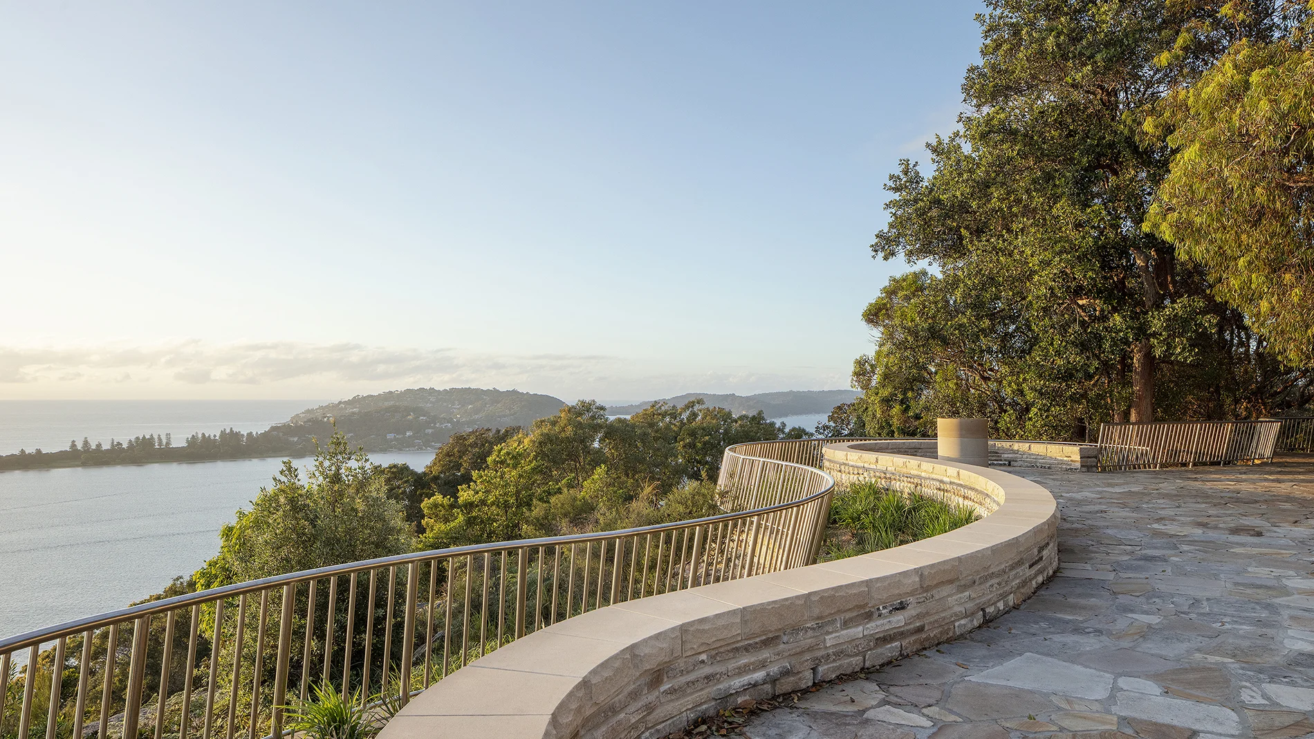A photograph of Sydney lookout with a curved sandstone wall and lower metal balustrade. There are trees above and below.