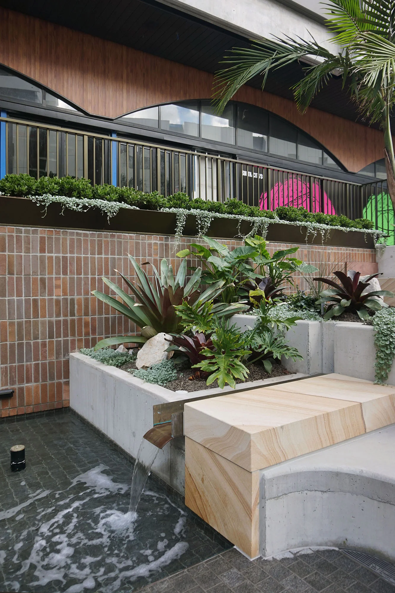 A photograph of water cascading down past stepped planters in a public plaza.