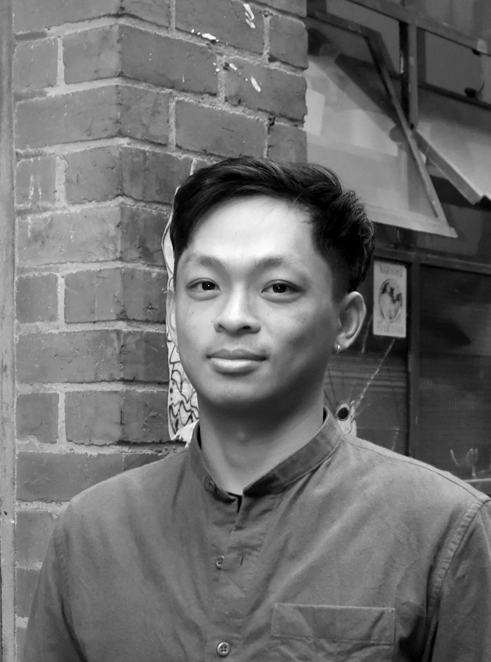 A black and white headshot of person in front of an urban wall.