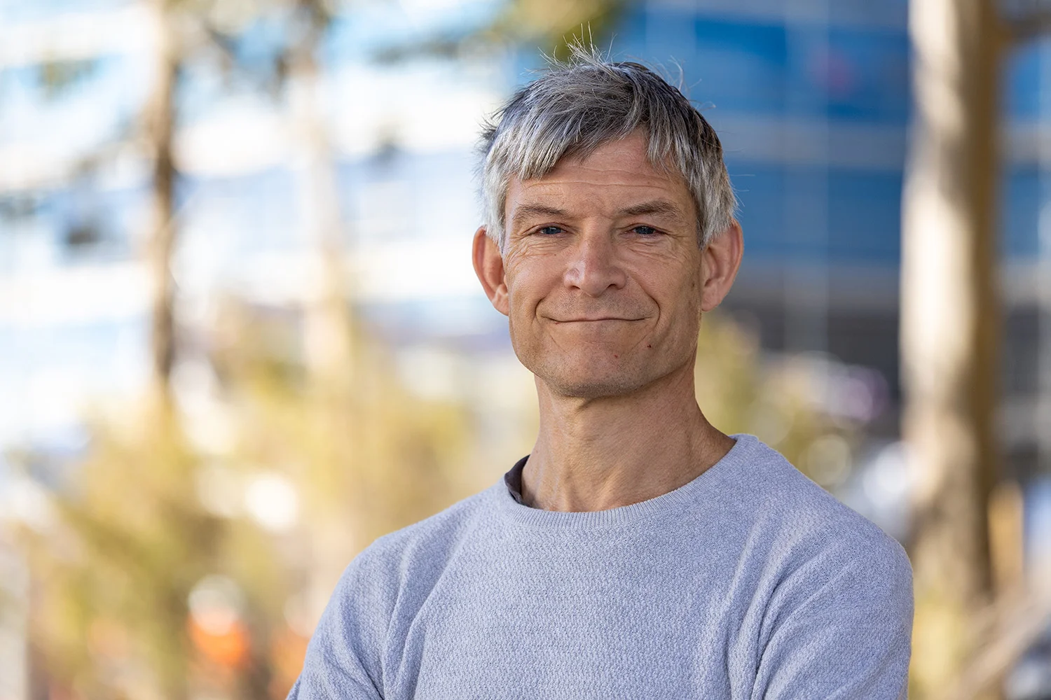 Man in grey casual sweater smiles at camera.