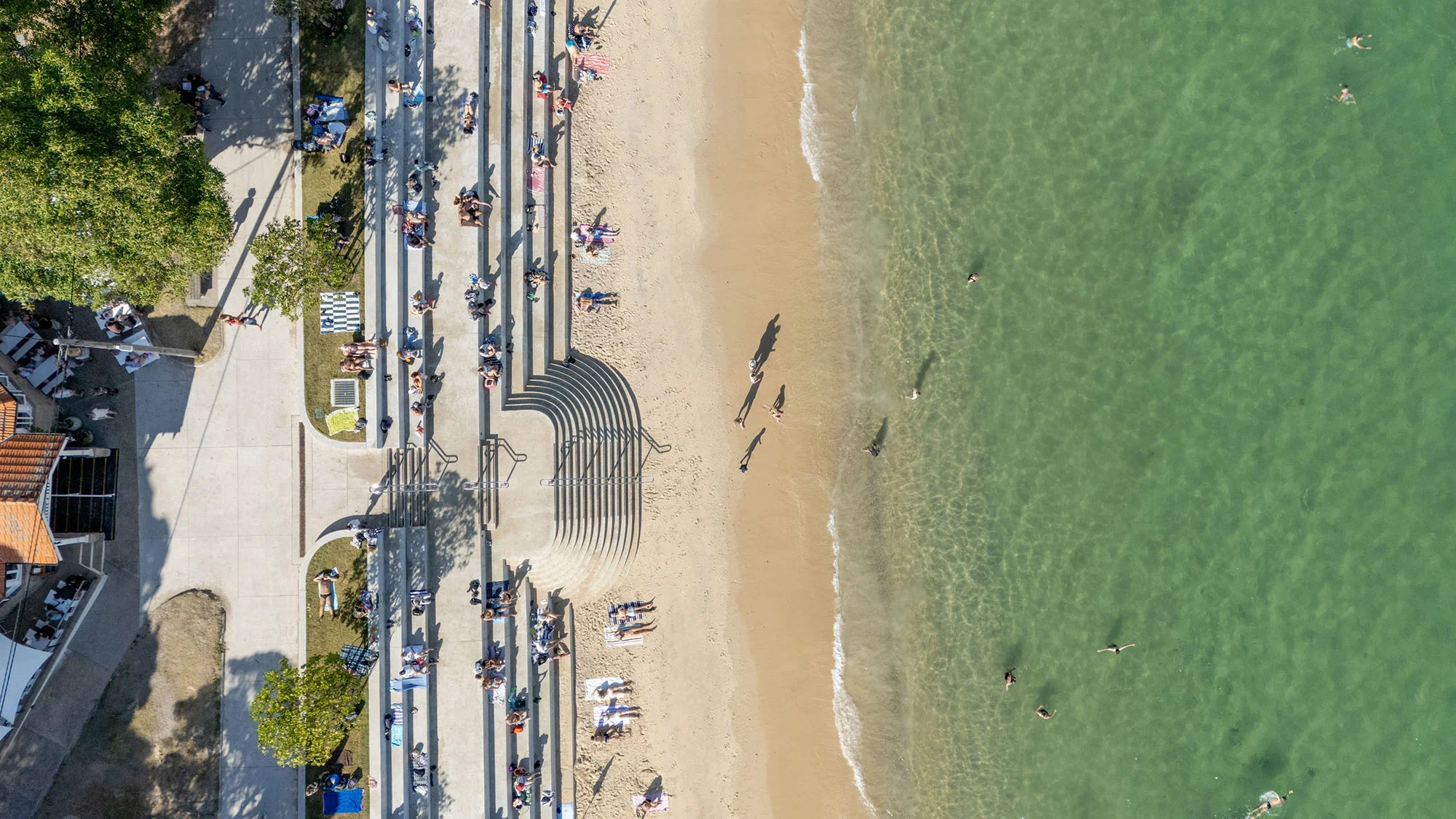 A drone photograph looking down on a sunny beach with a tiered seawall.