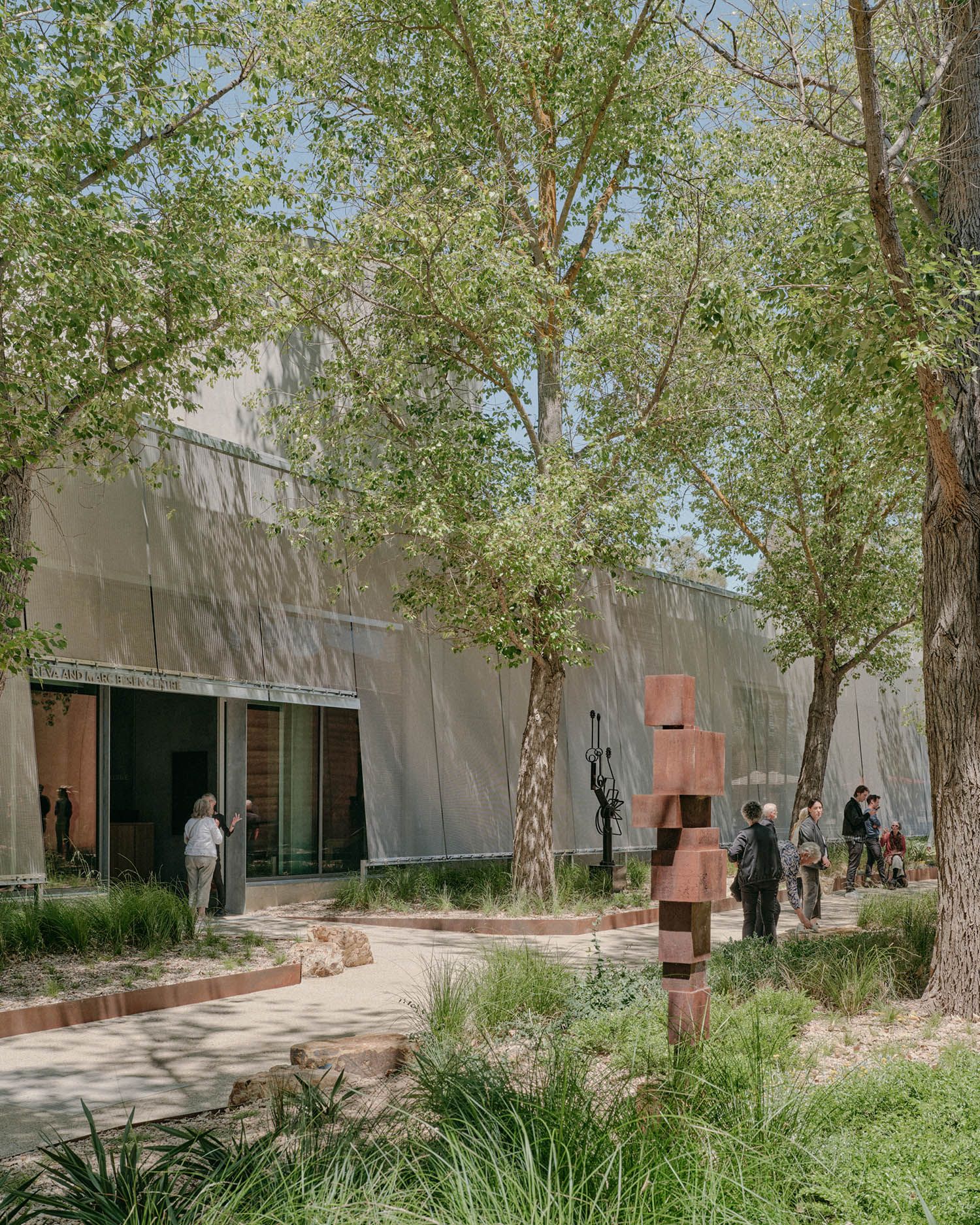 A photo of an art gallery entrance surrounded by trees. There are people and sculptures standing outside.