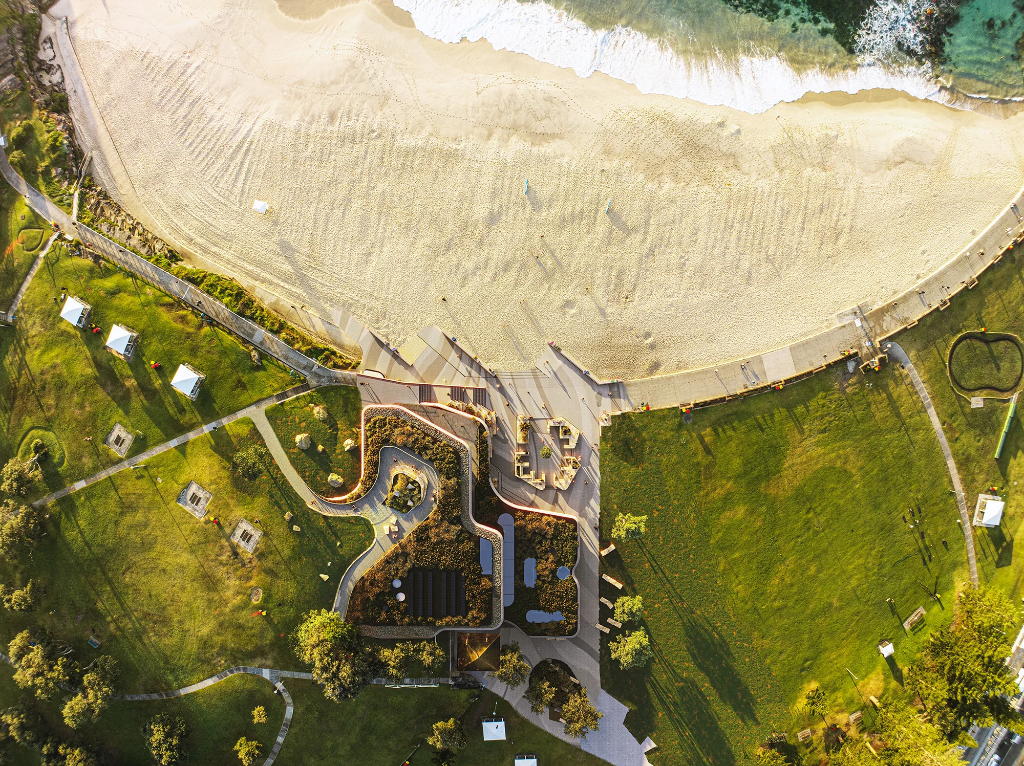 A digital render of a beach, viewed from above, with a contemporary surf life saving club embedded in the landscape.