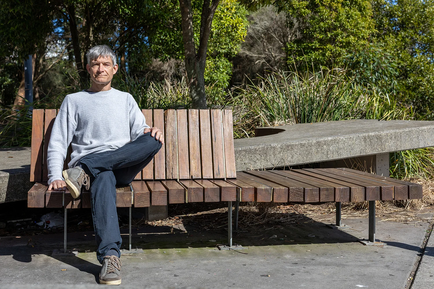 Man in casual clothes sits on a wooden park bench.