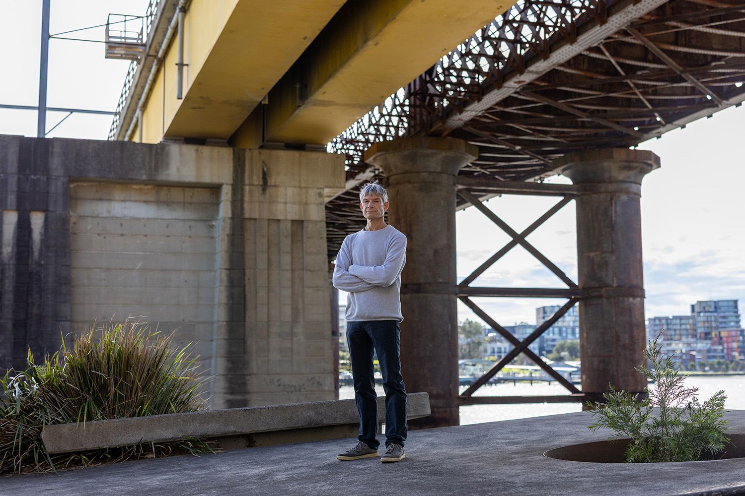 Man in casual clothes stands under bridge.