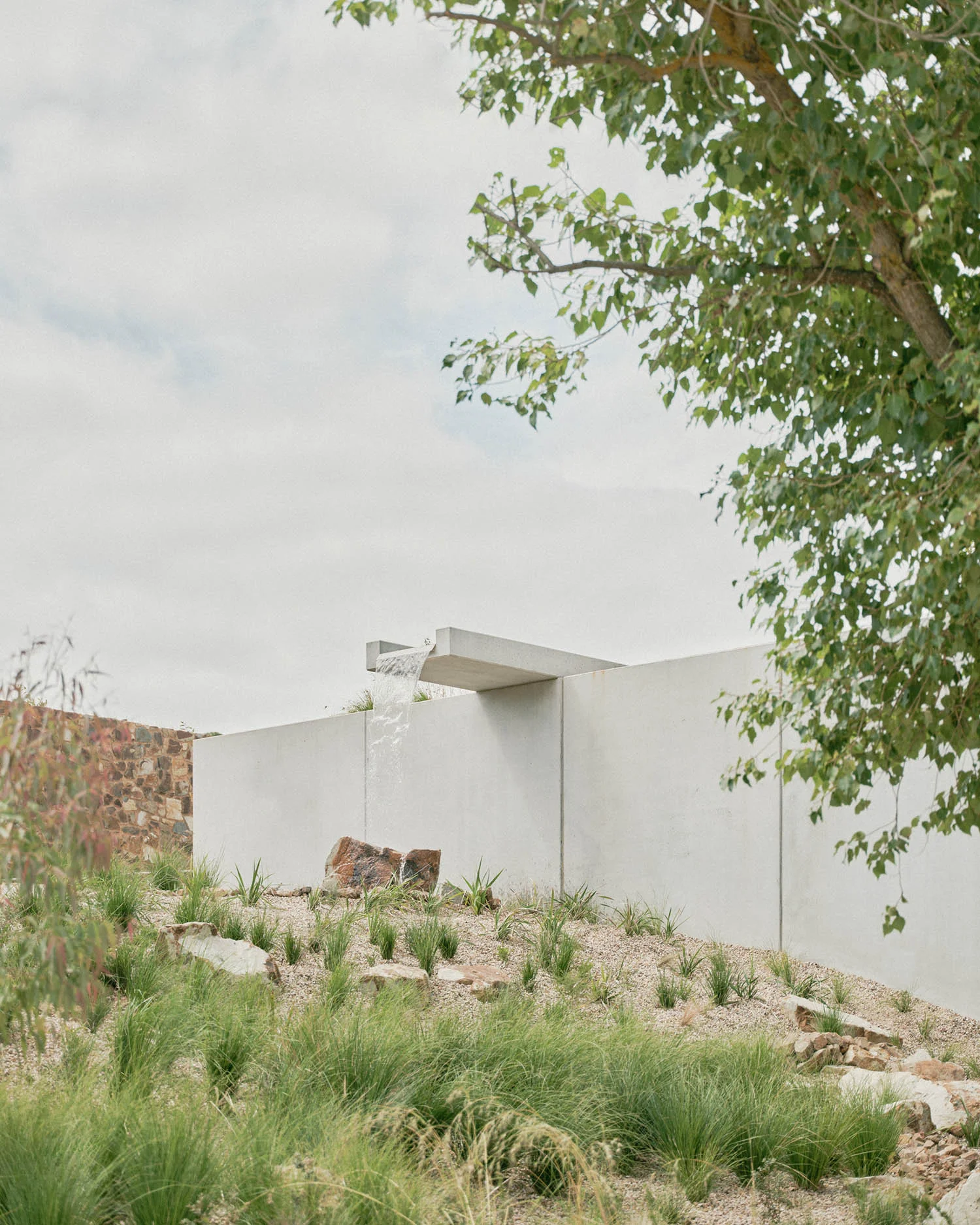 A photograph of a falling water feature. Waterflows onto a rock, set in a landscape filled with grasses.