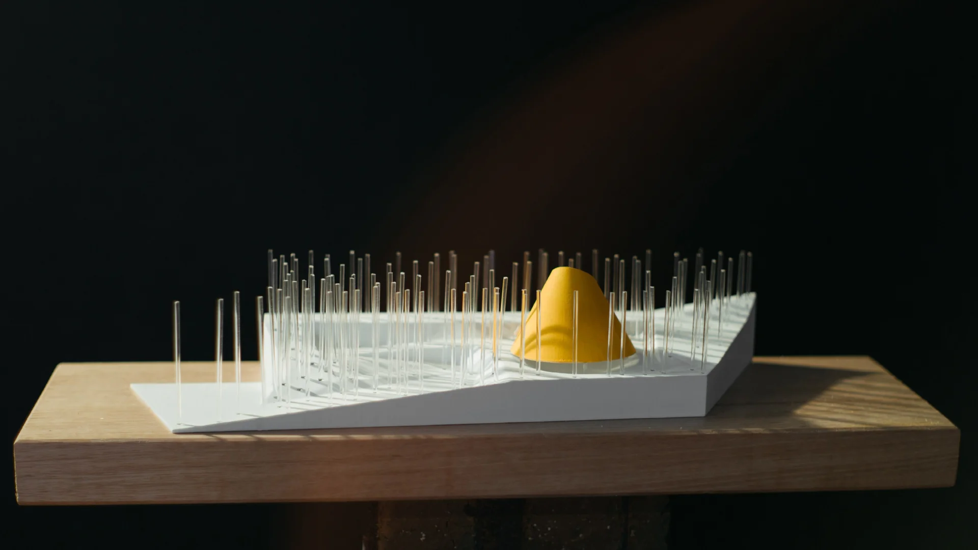 A photo of an architectural model, with a pop of yellow, on a piece of timber.