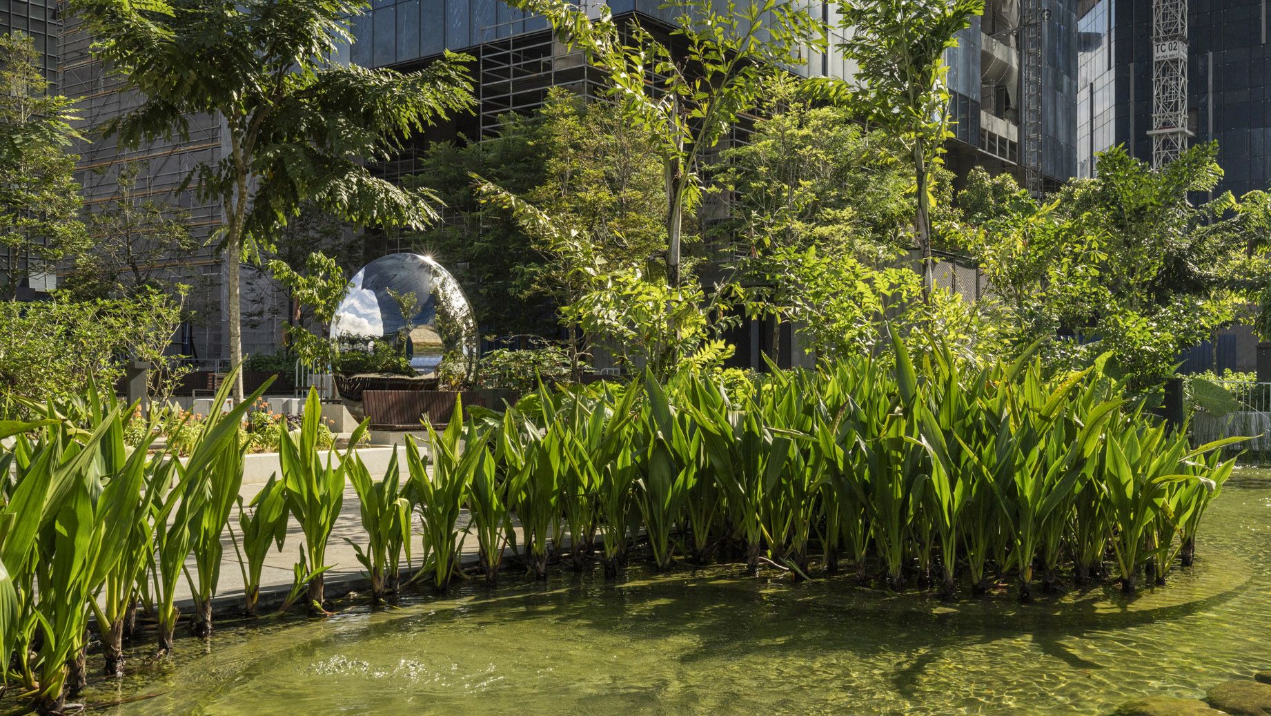 A photo of a lush rooftop garden with a large area of water, and a silver sculpture.