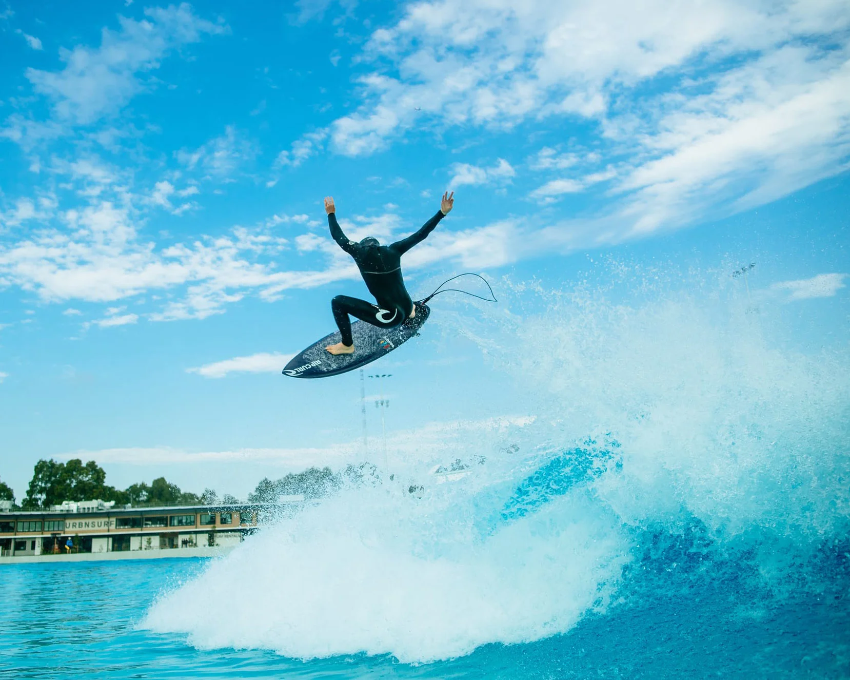 A surfer in mid-air above a wave pool.