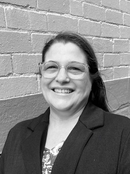 A black and white headshot of a smiling person in front of a brick wall.