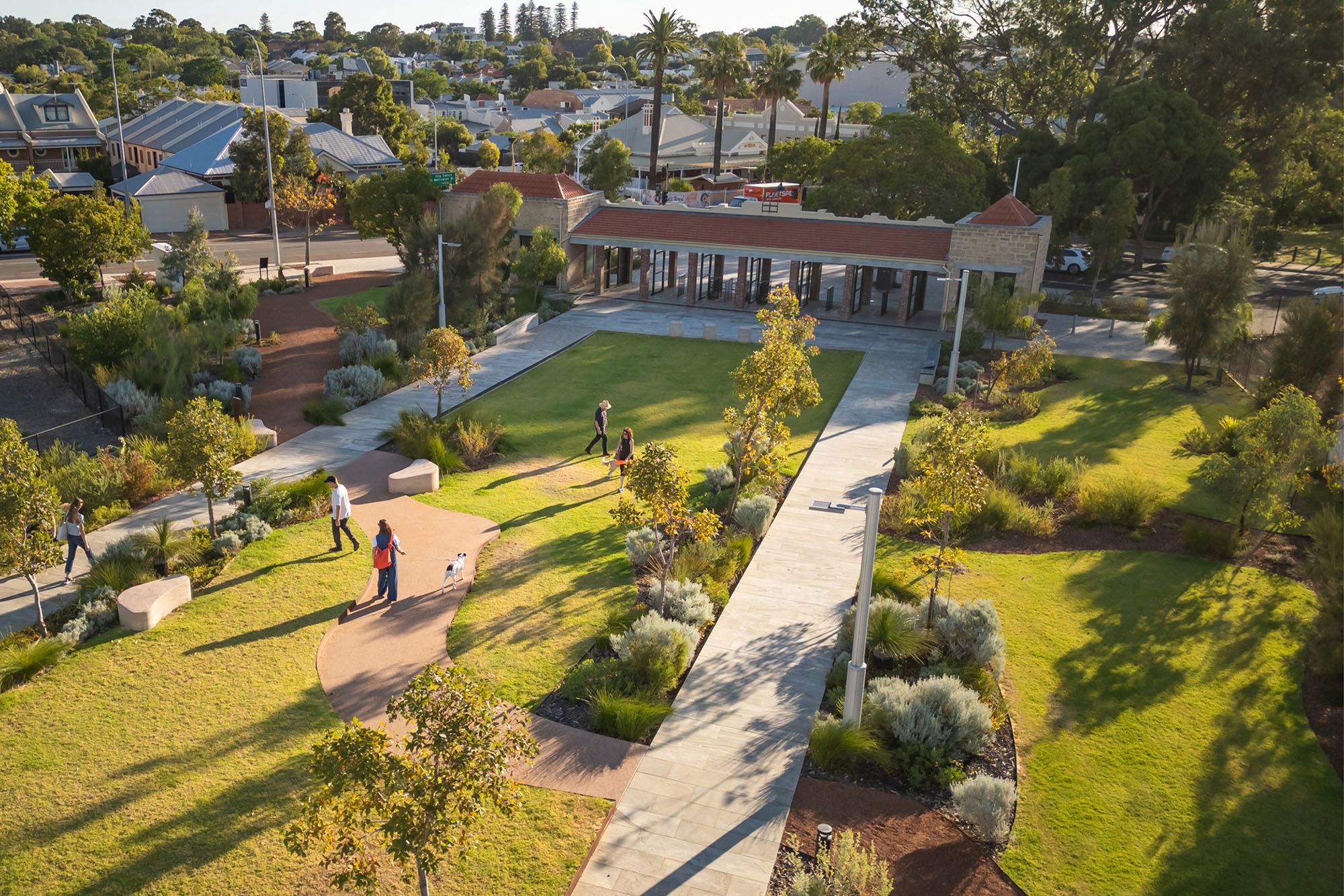 An aerial photograph of a handful of people walking around a park with paved paths, lawn area, and Australian native plants.