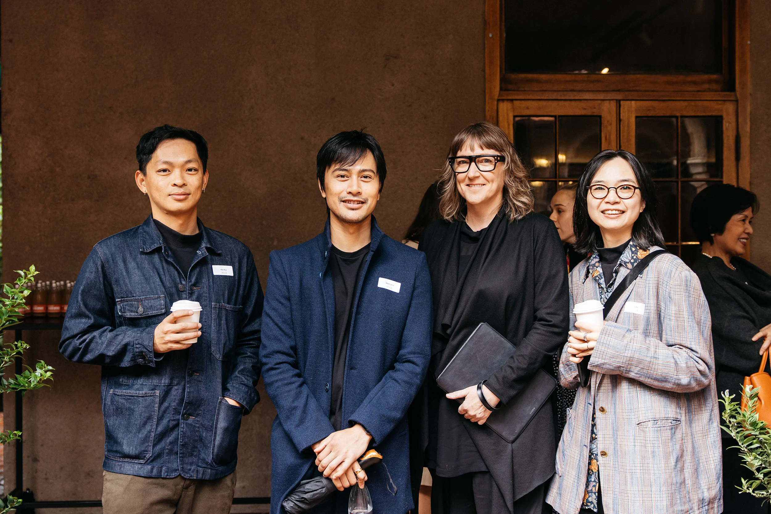 A photo of four people smiling for the camera. Two are holding cups of coffee.
