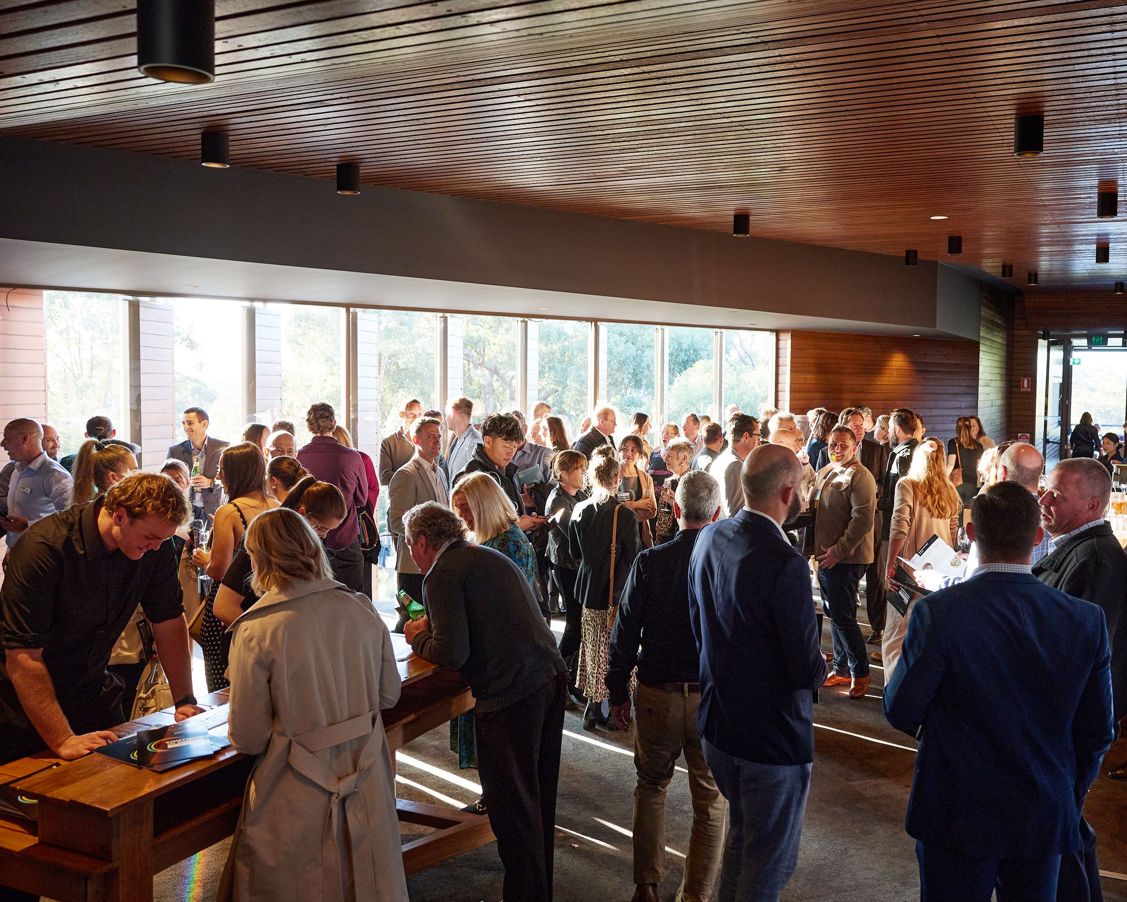 A photo of a large group of people gathering beside large windows in an event space. 