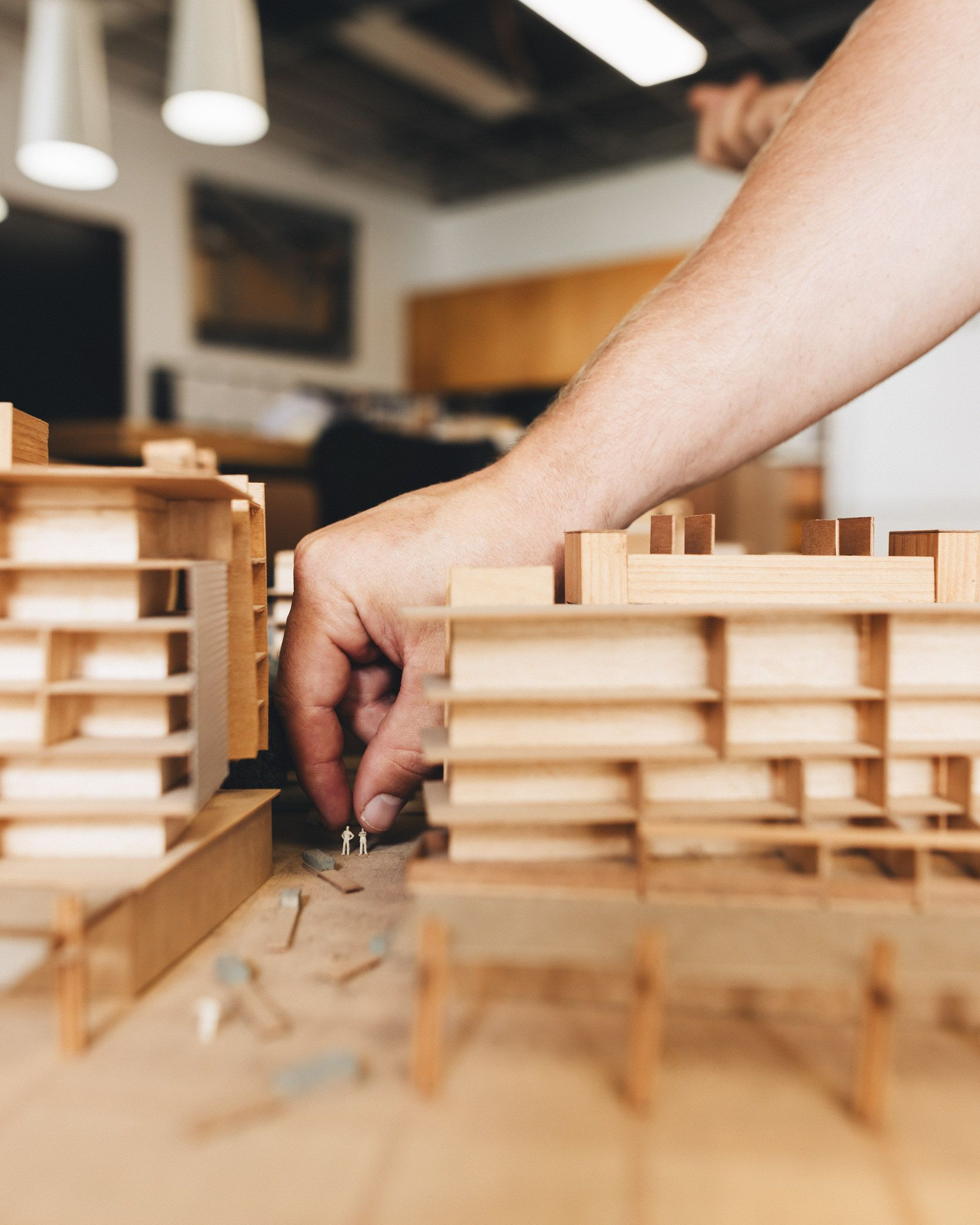 A photograph of a hand moving two small figures within a large timber architectural model. 