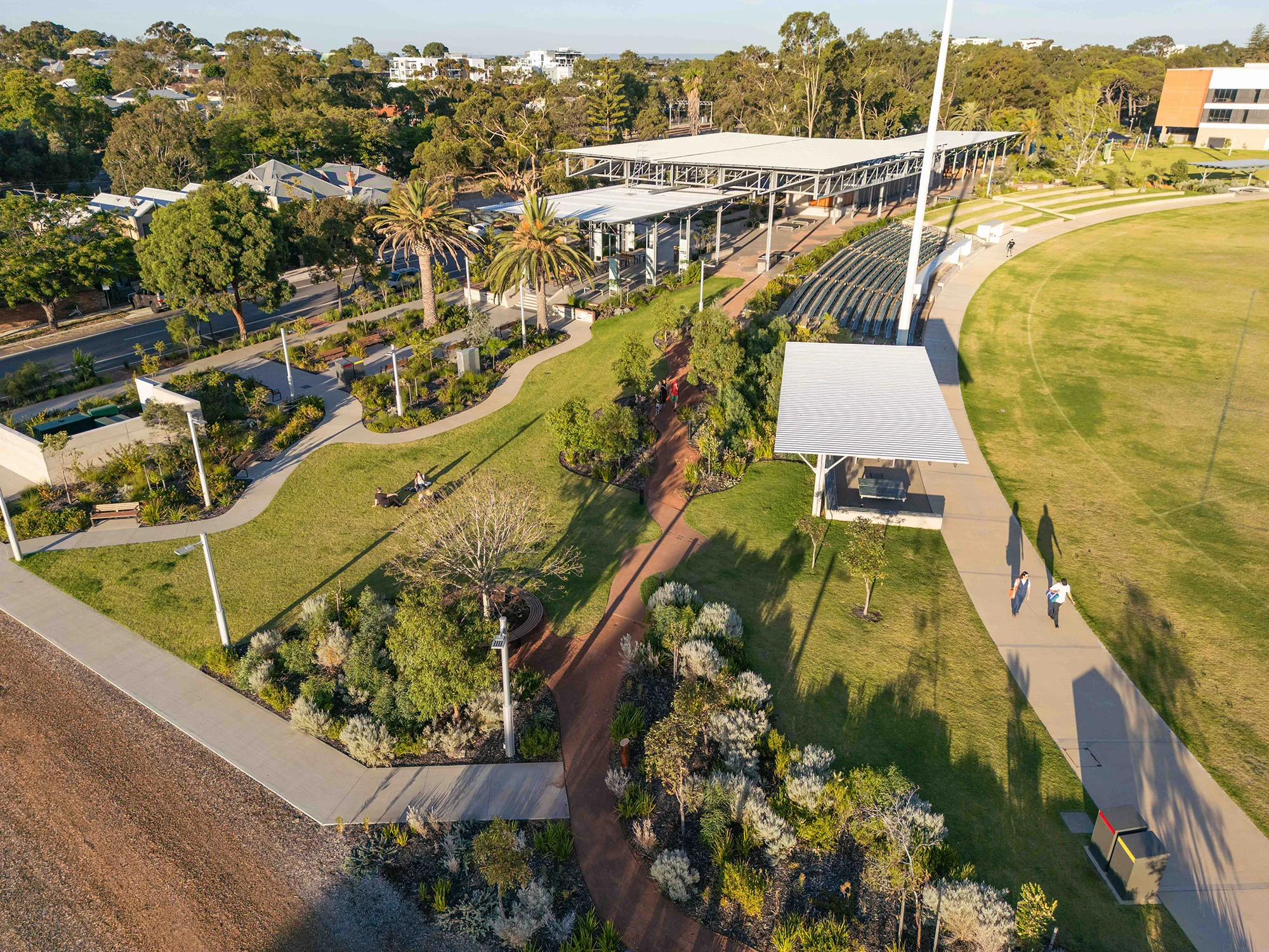 A photo of a park taken with a drone. There are winding paths, lawn areas, garden beds, and shade structures.