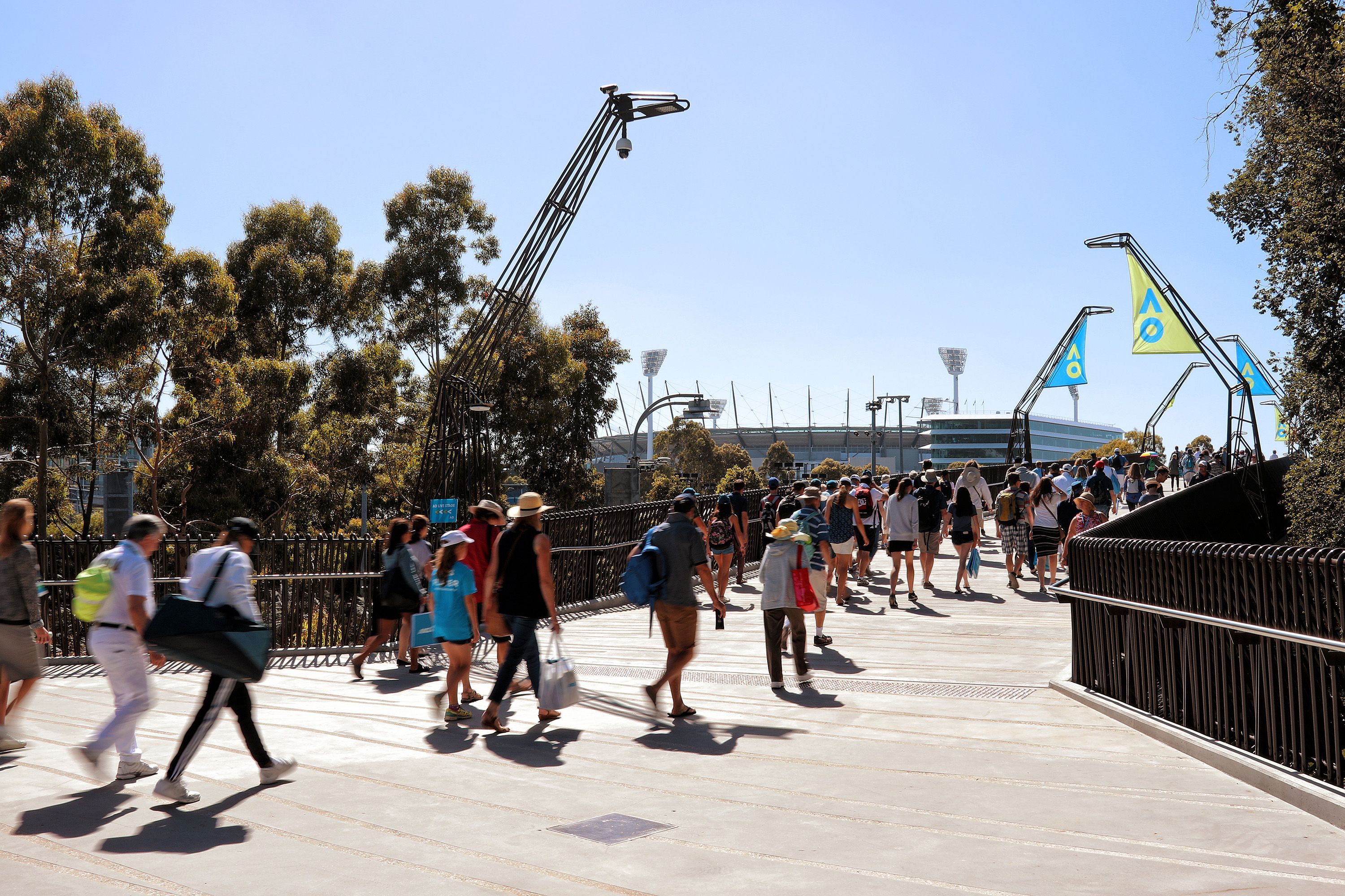 A photograph of crowds of people crossing a pedestrian bridge on a sunny day.