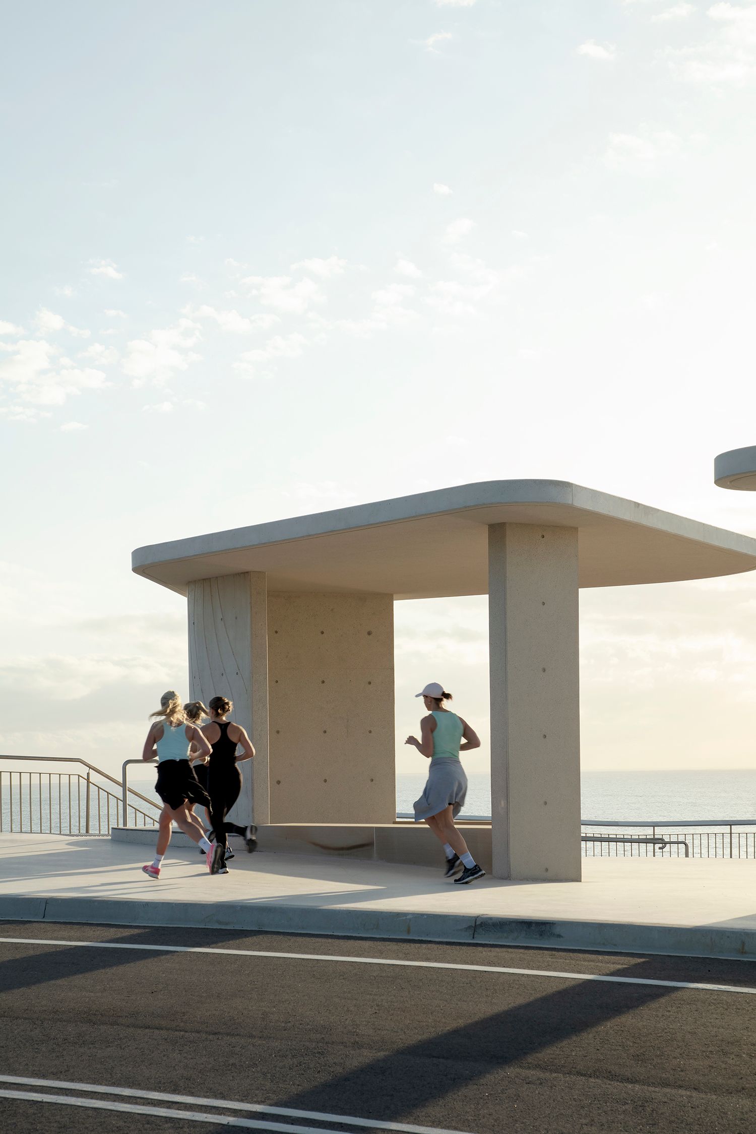 An early morning photograph of three runners, passing a concrete viewing shelter. 