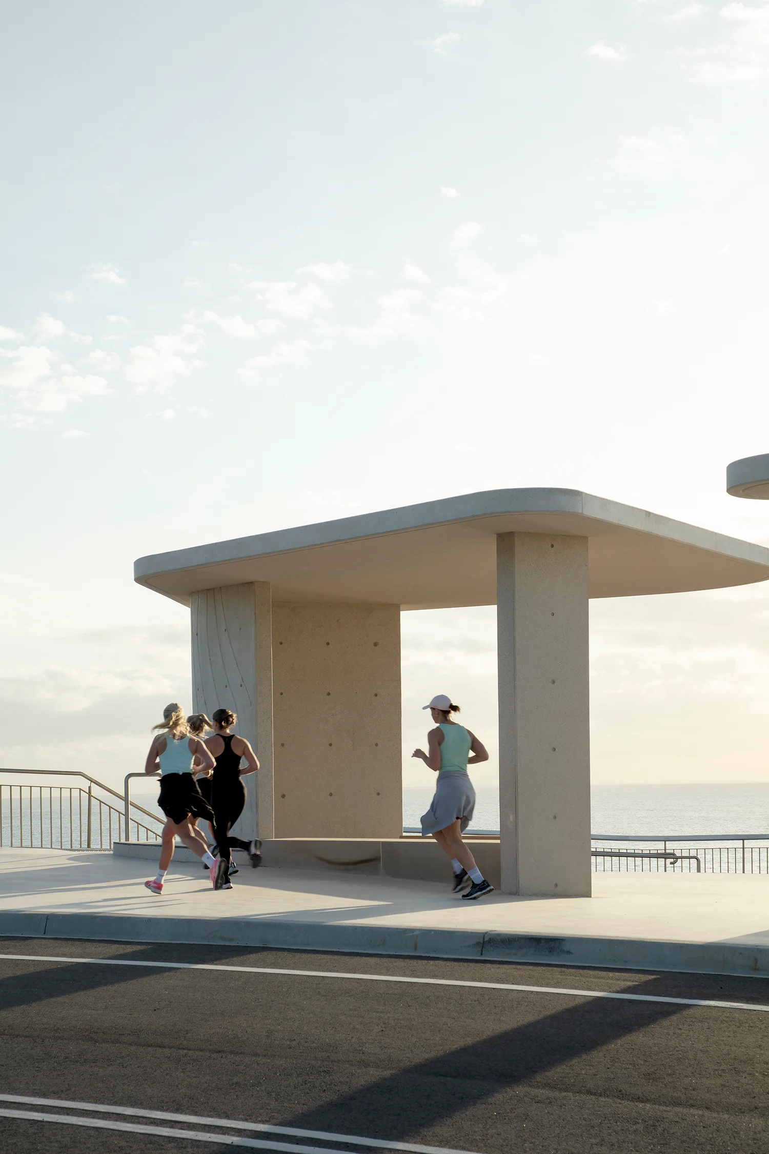 An early morning photograph of three runners, passing a concrete viewing shelter.