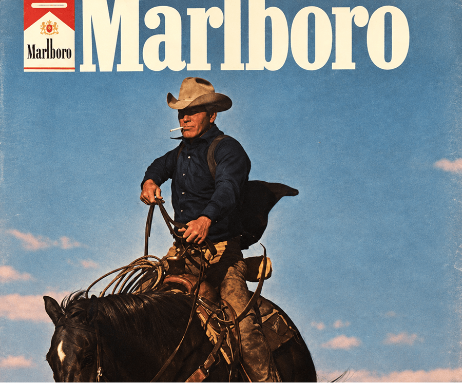 Classic Marlboro Man print ad created by Leo Burnett, showing a cowboy on horseback with a lasso under a blue sky