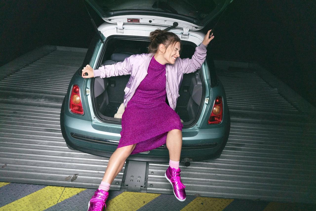 Woman in purple dress and shoes sitting in the trunk of the car