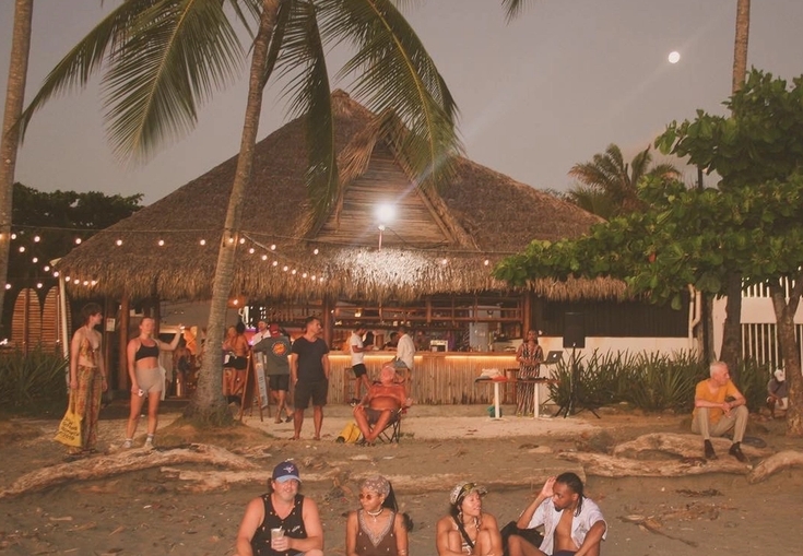 en gruppe mennesker sitter på stranda foran en hytte