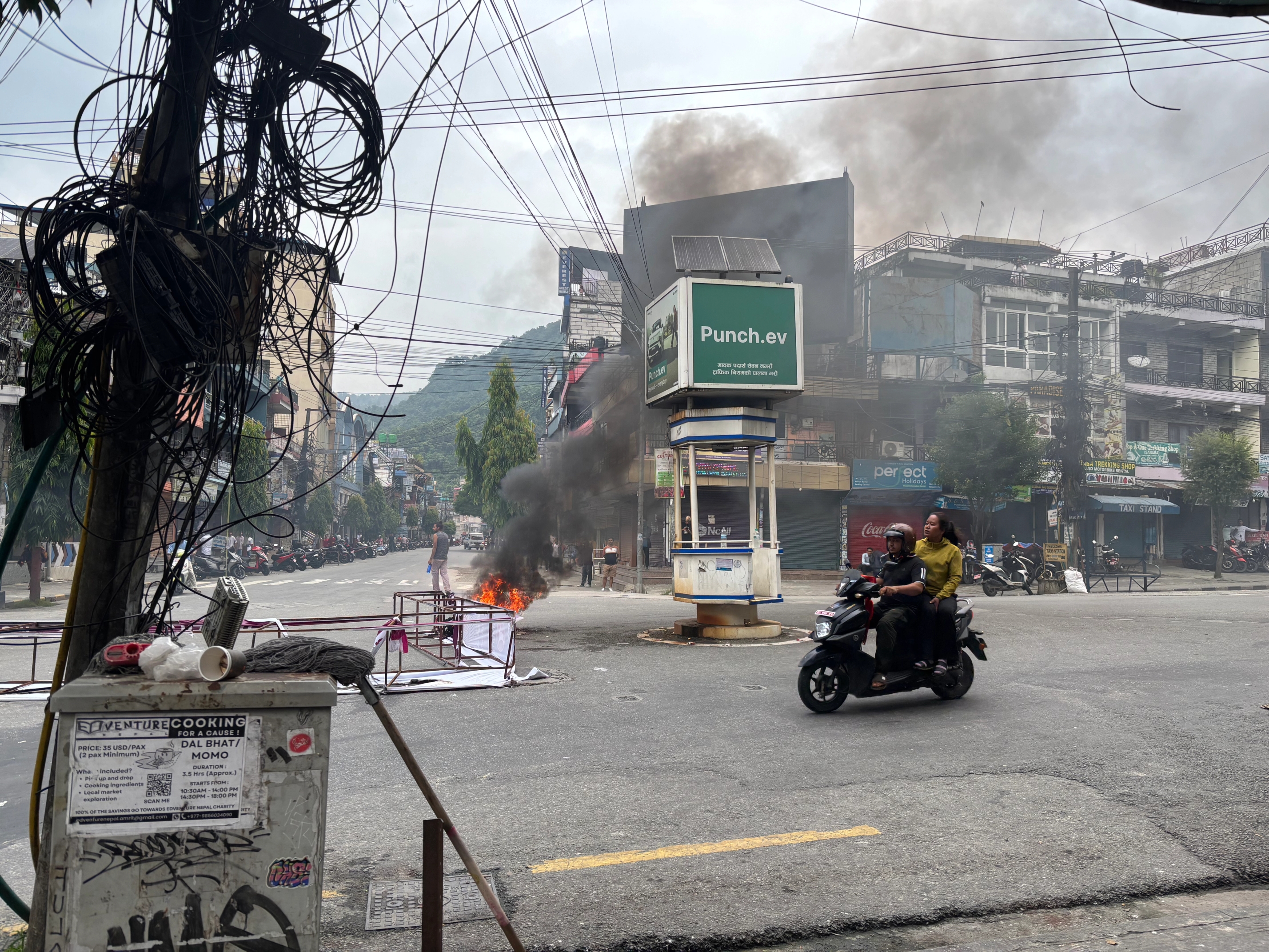a man is riding a motorcycle down a street with smoke coming out of a building .