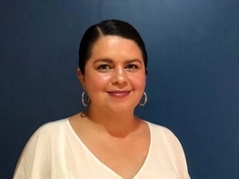 a woman wearing a white shirt and earrings is standing in front of a blue wall .