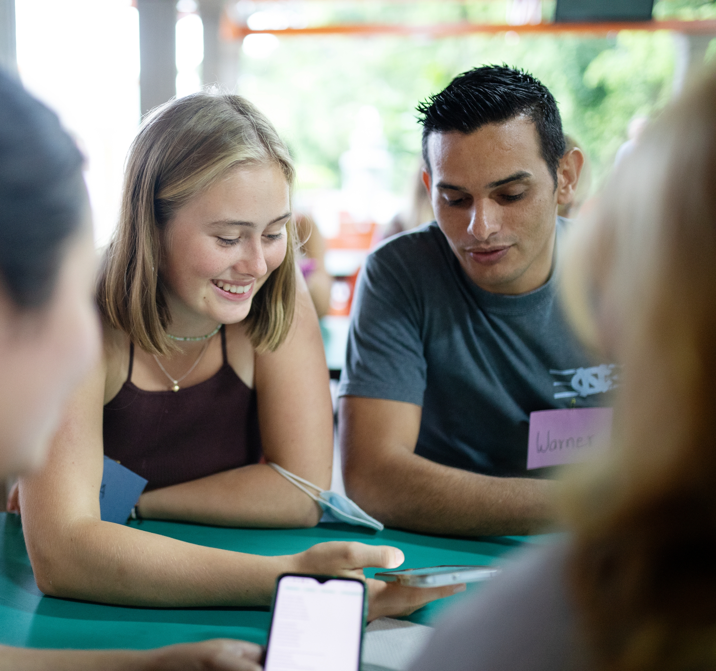 a group of people are sitting at a table looking at a cell phone .