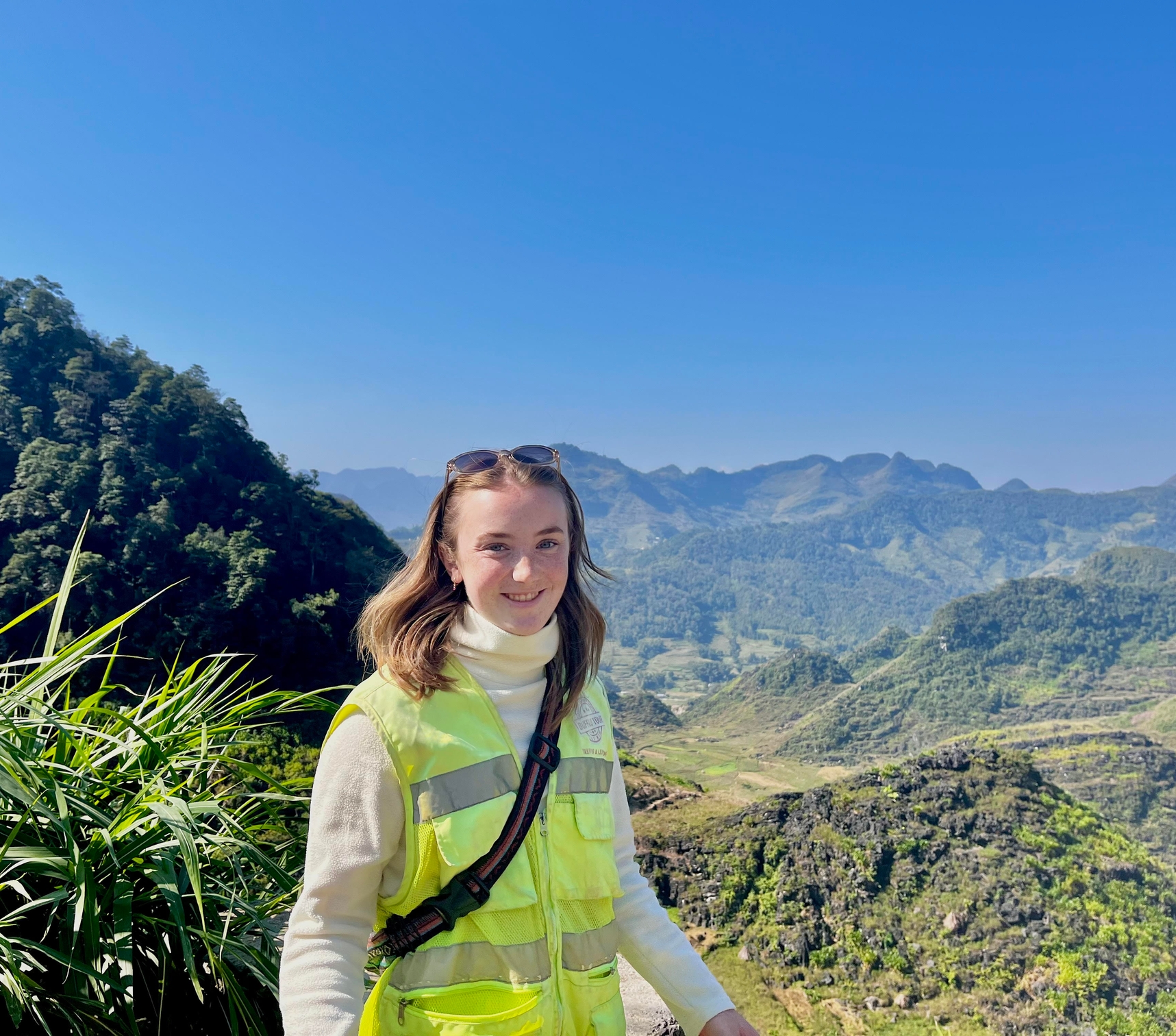 a woman in a yellow vest is standing on top of a mountain .